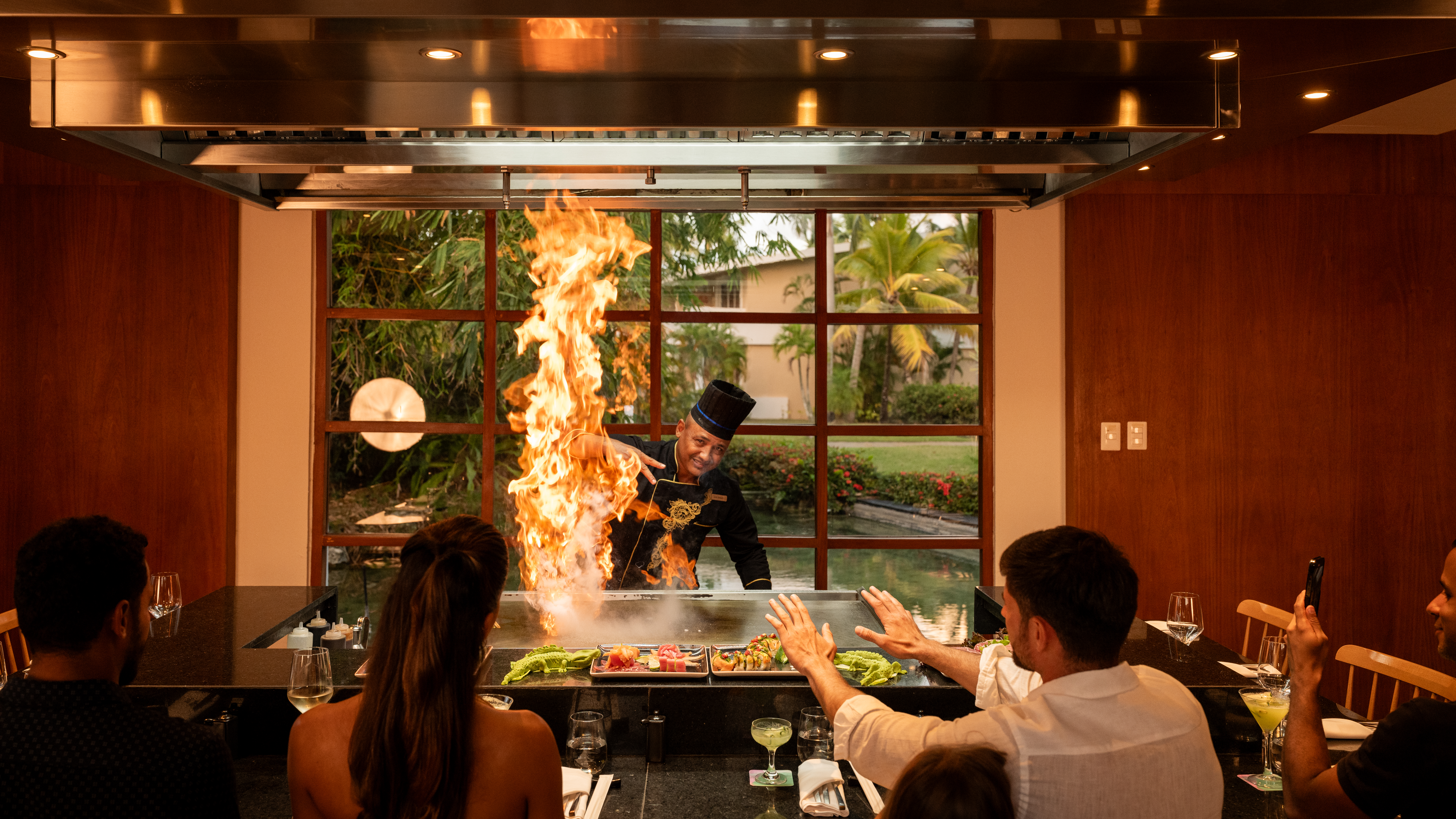 Chef ignites large flames cooking teppanyaki for restaurant diners.