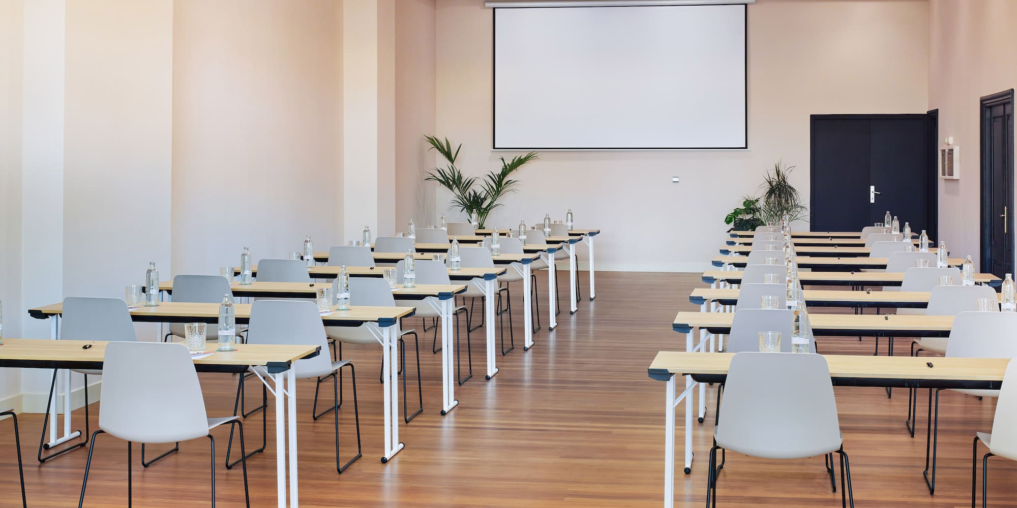Modern conference room with projector screen, rows of tables and chairs.