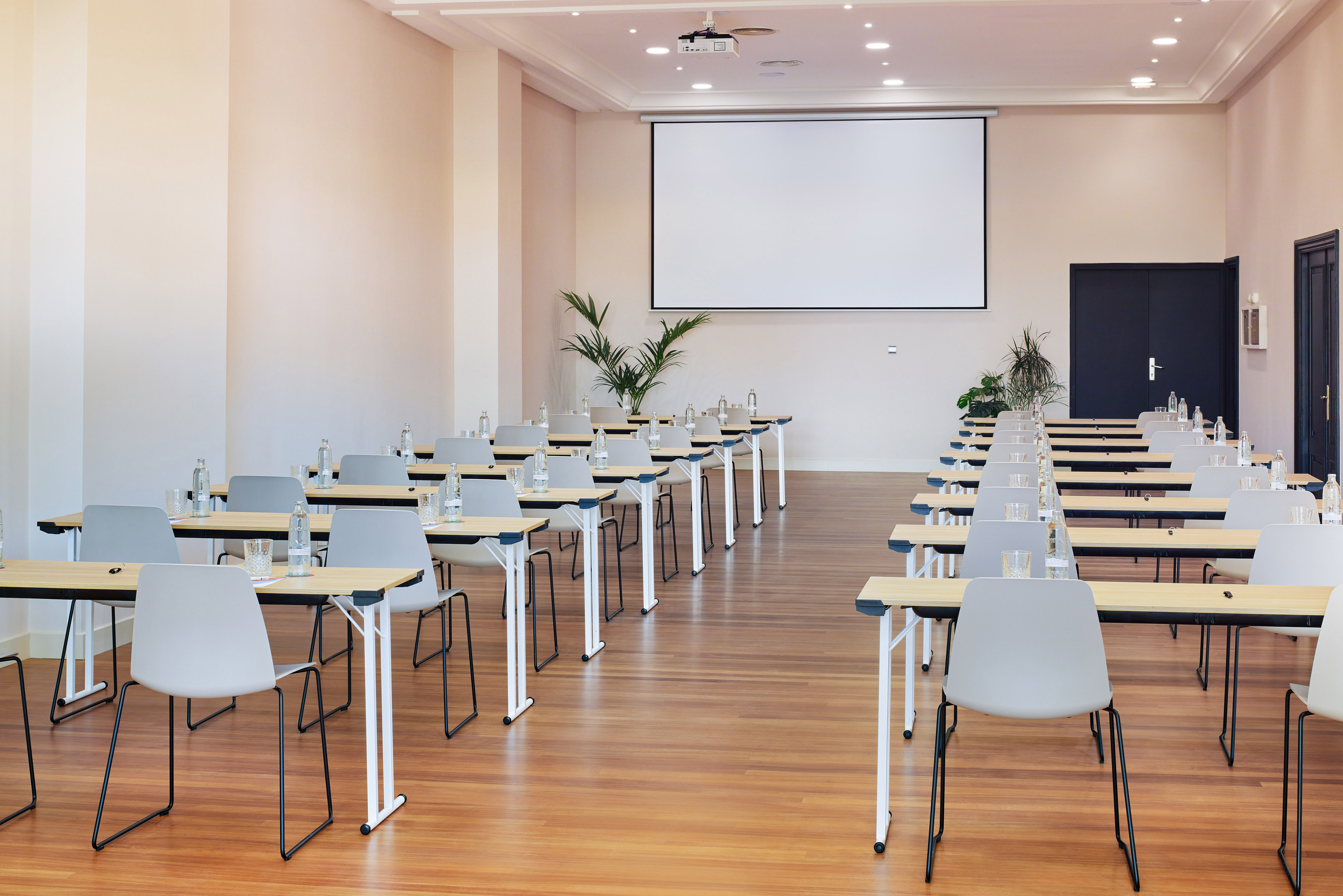 Modern conference room with projector screen, rows of tables and chairs.