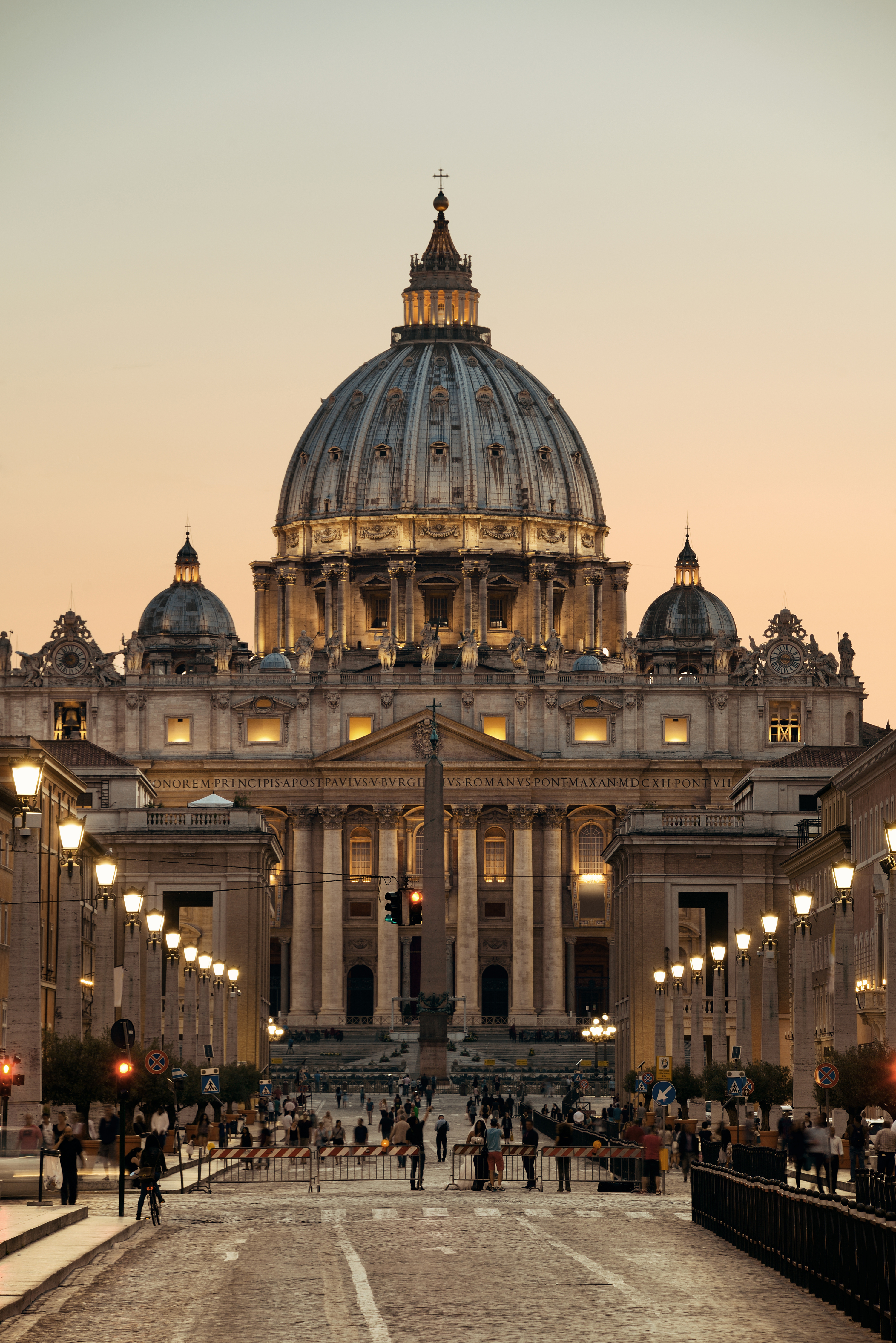 a large building with a dome and people walking in the street with St. Peter's Basilica in the background