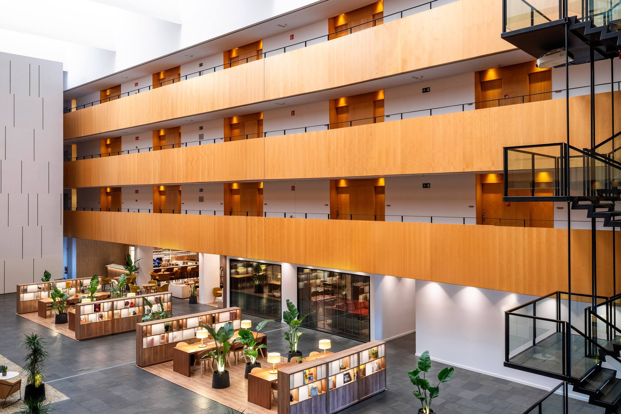 Modern hotel atrium with wood-paneled levels, black staircase, and stylish lounge areas.