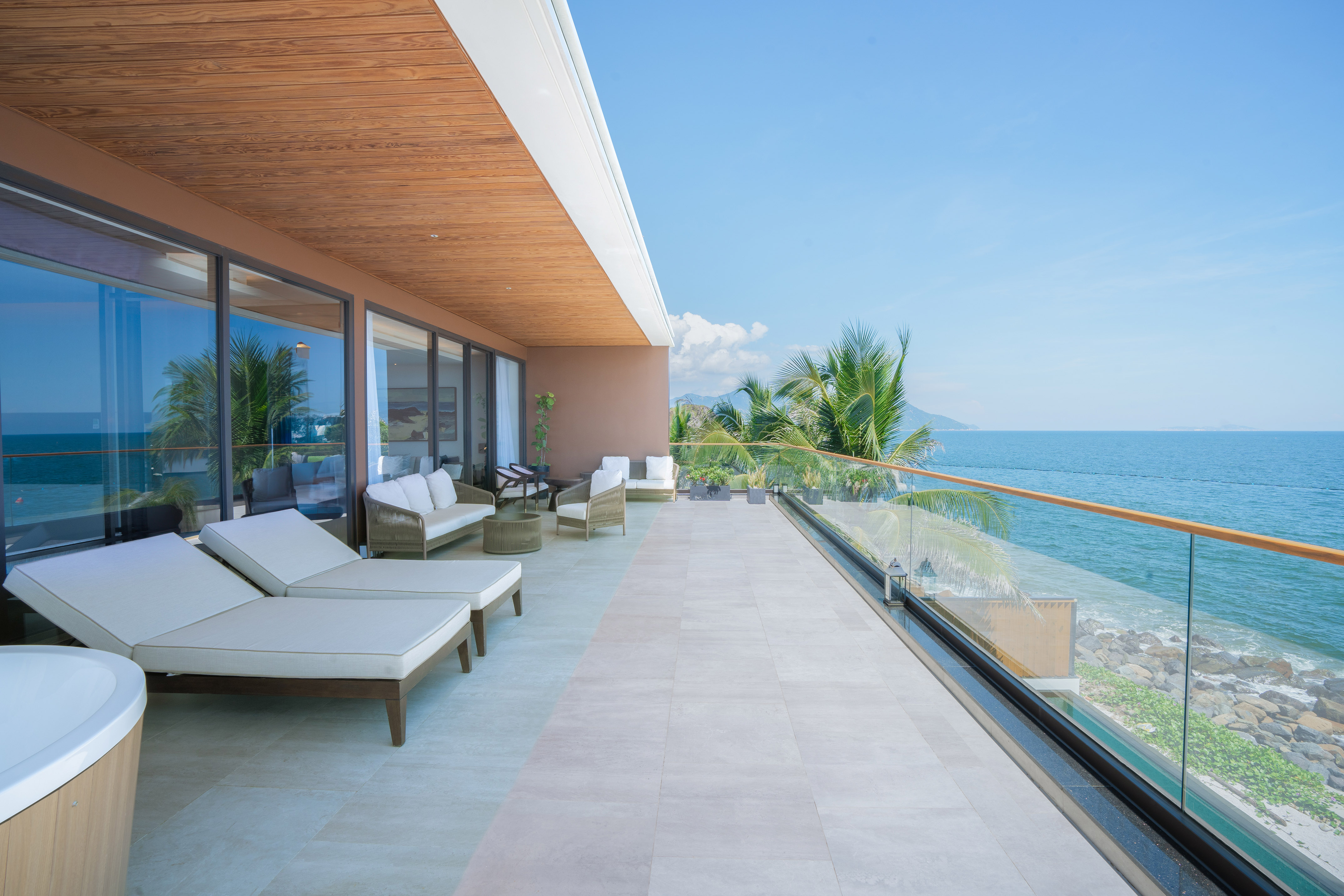 Luxury ocean view balcony with modern lounge chairs and palm trees.