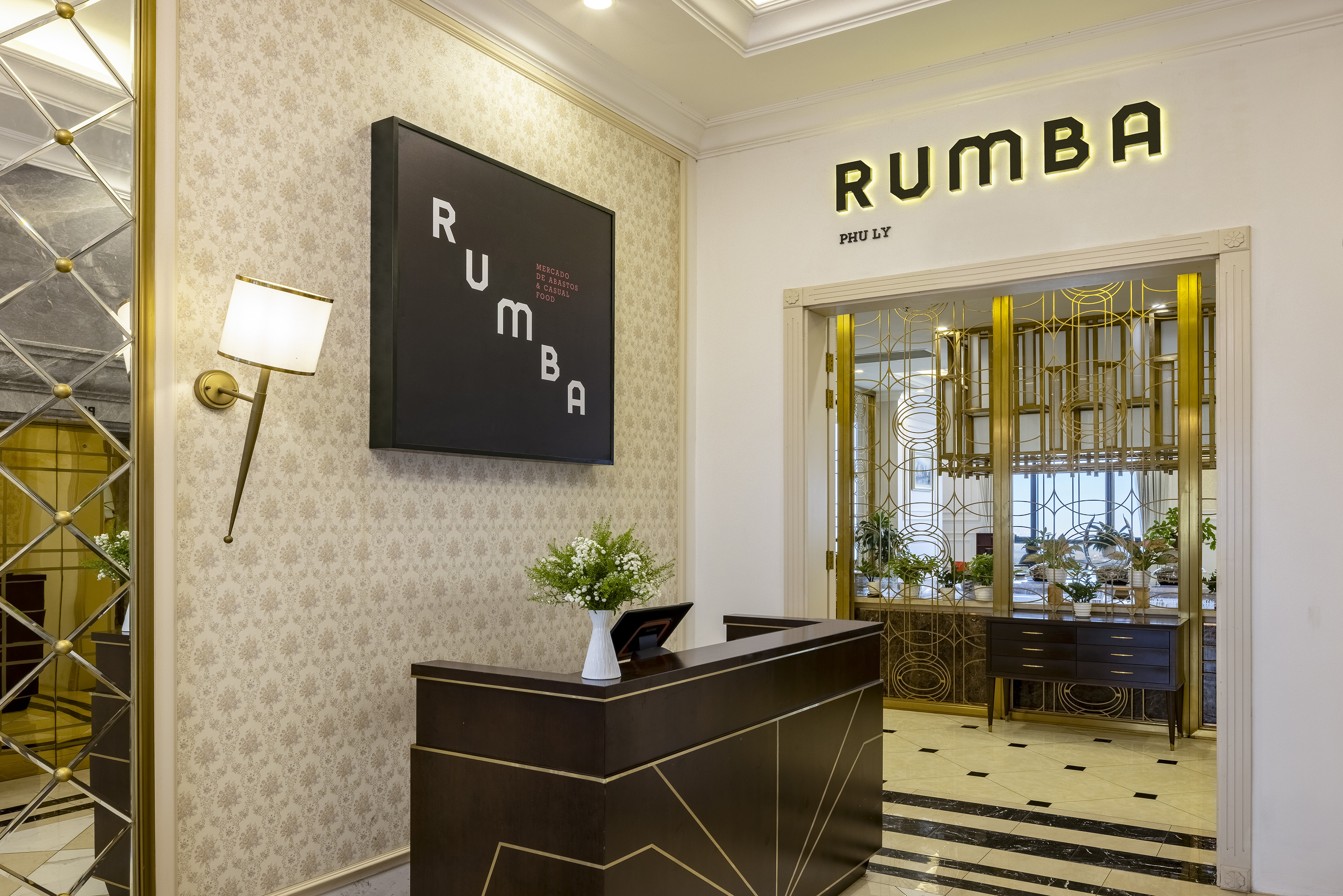 Rumba restaurant entrance, illuminated sign, dark reception desk, gold decor.