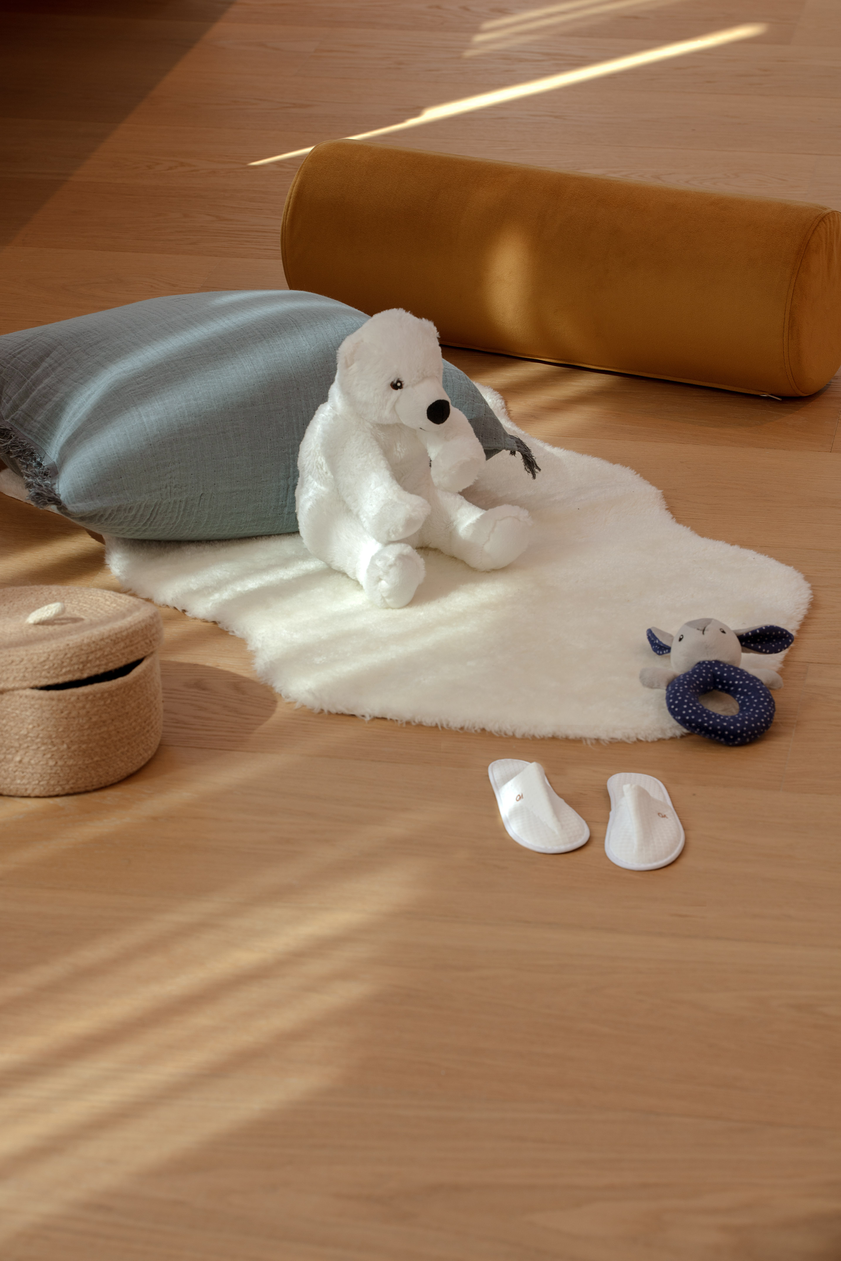 Cozy baby nursery decor: teddy bear, slippers, and soft rug on wood.