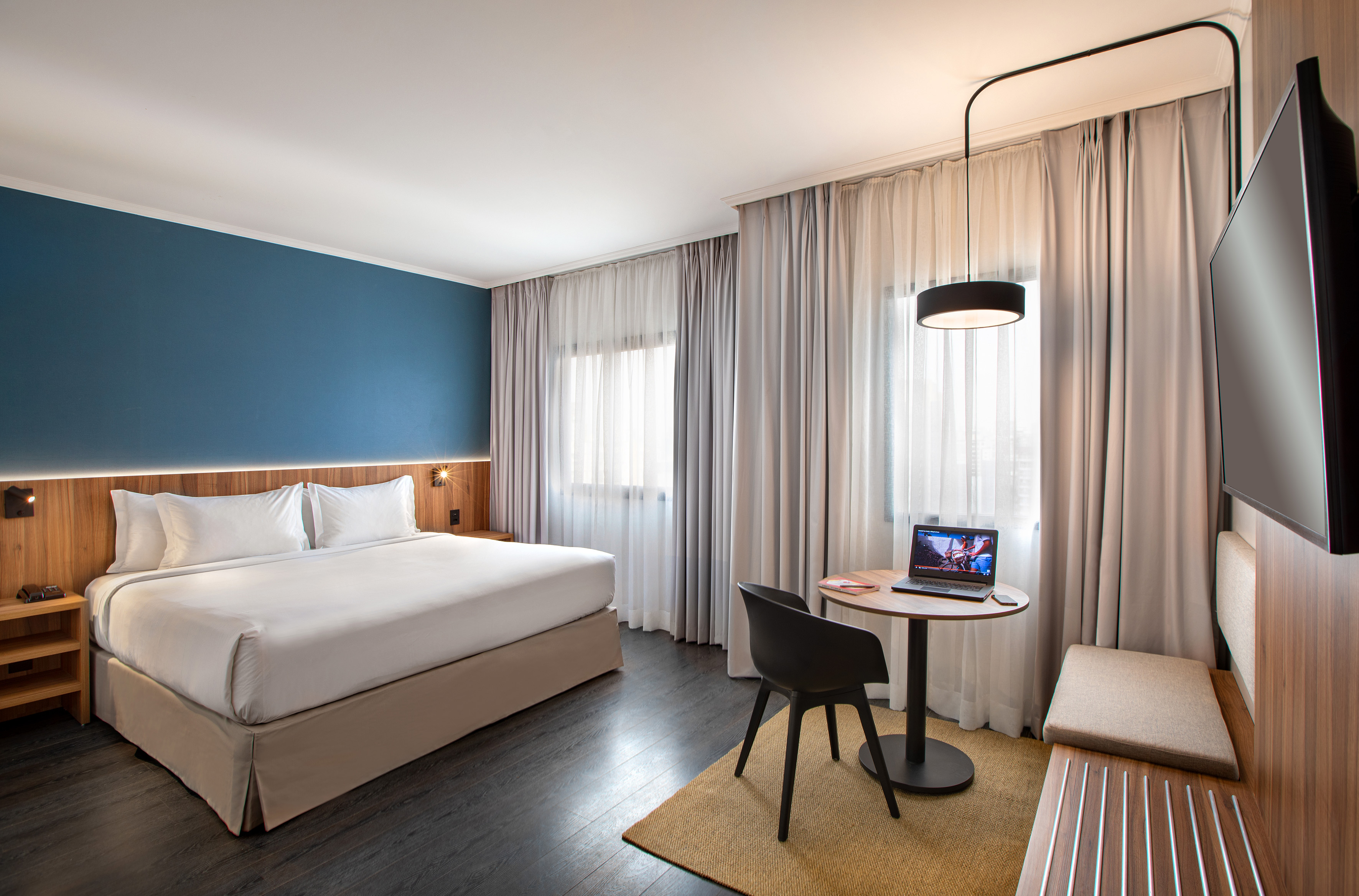Modern hotel room with king bed, blue accent wall, workspace, and TV.