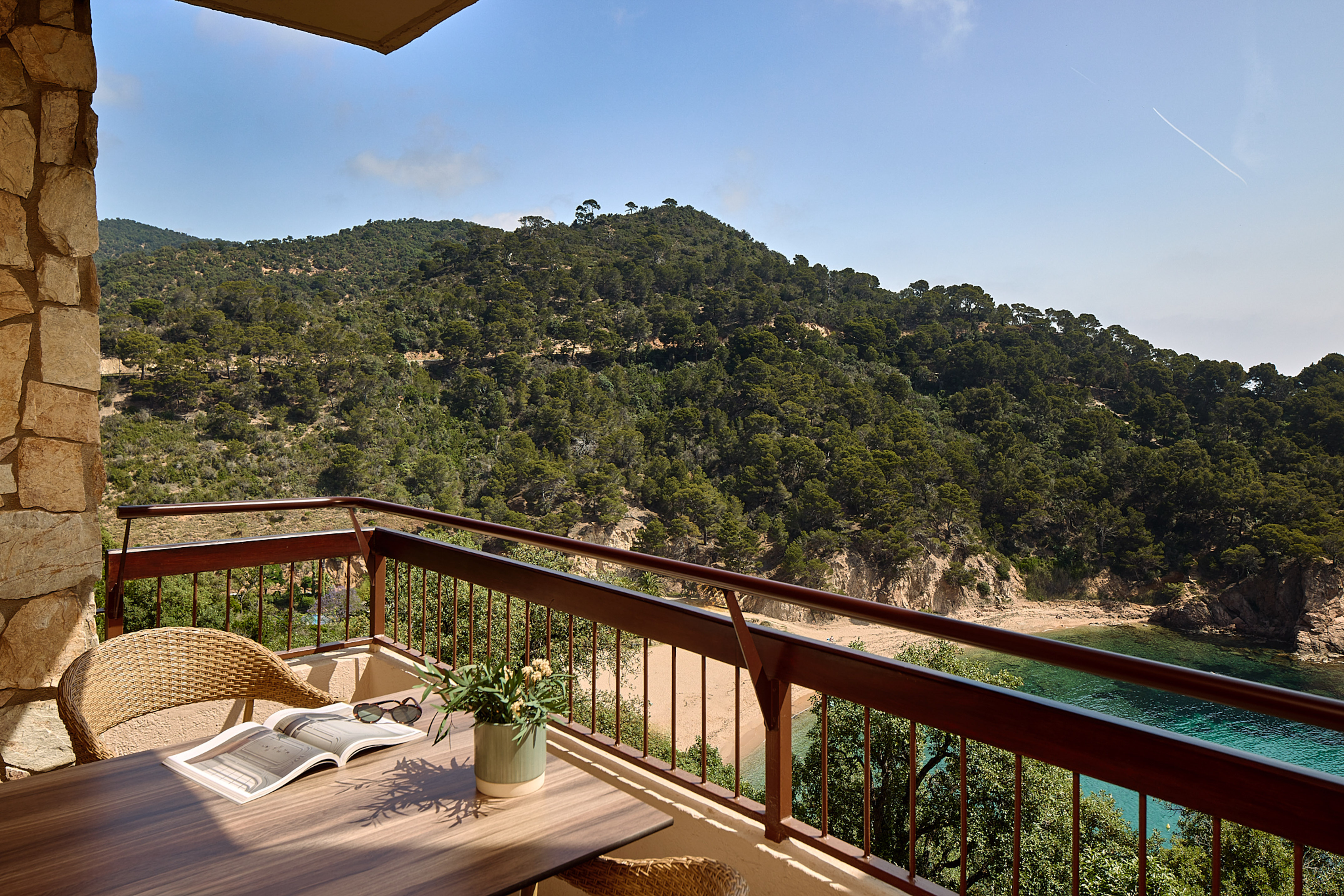 Scenic balcony with Mediterranean sea view, forested hills, and sandy beach.