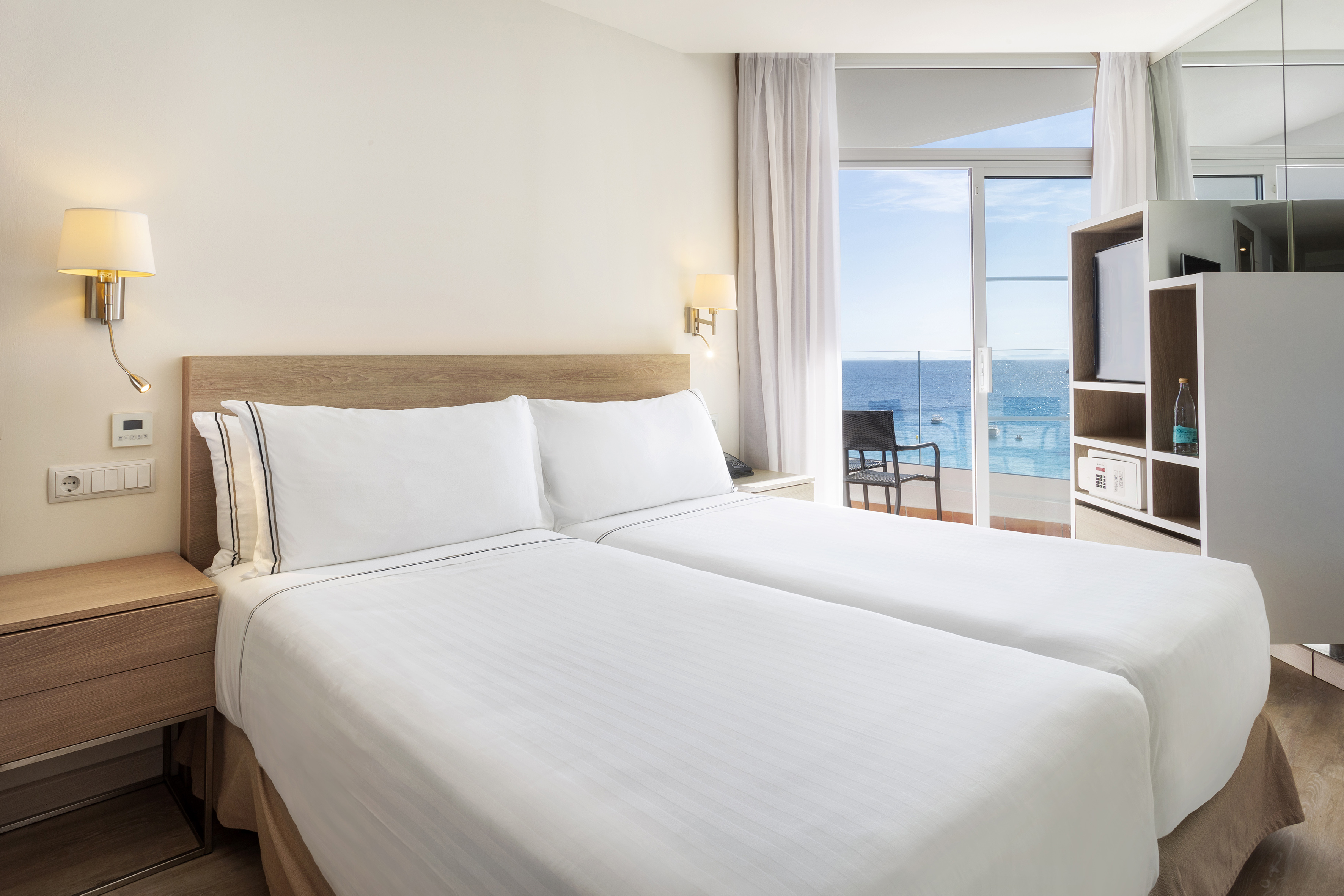 Modern hotel room with twin beds and ocean view balcony.