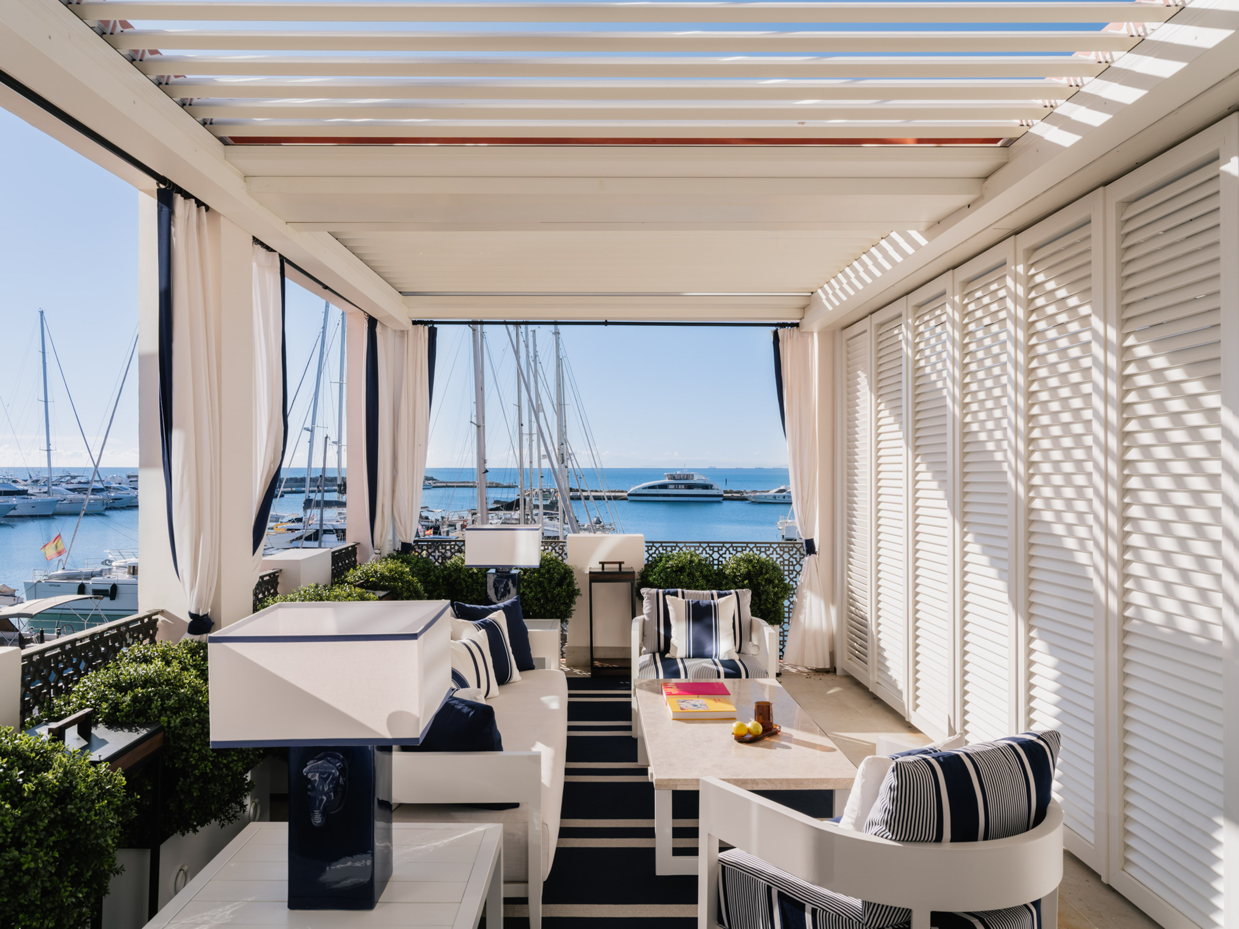 Outdoor terrace with marina view, white pergola, and blue nautical furniture.