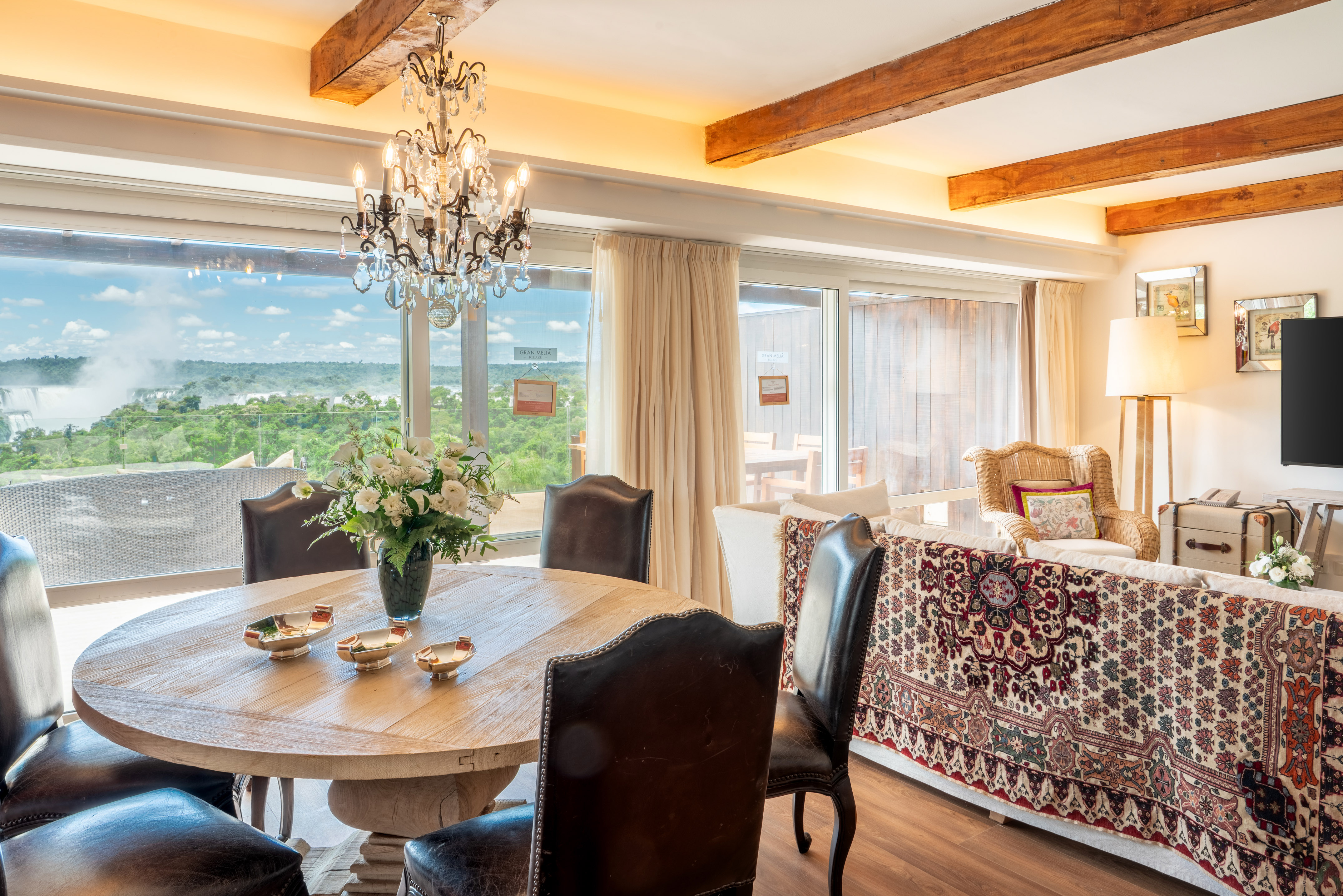 Luxury suite with Iguazu Falls view, dining table, leather chairs, and chandelier.