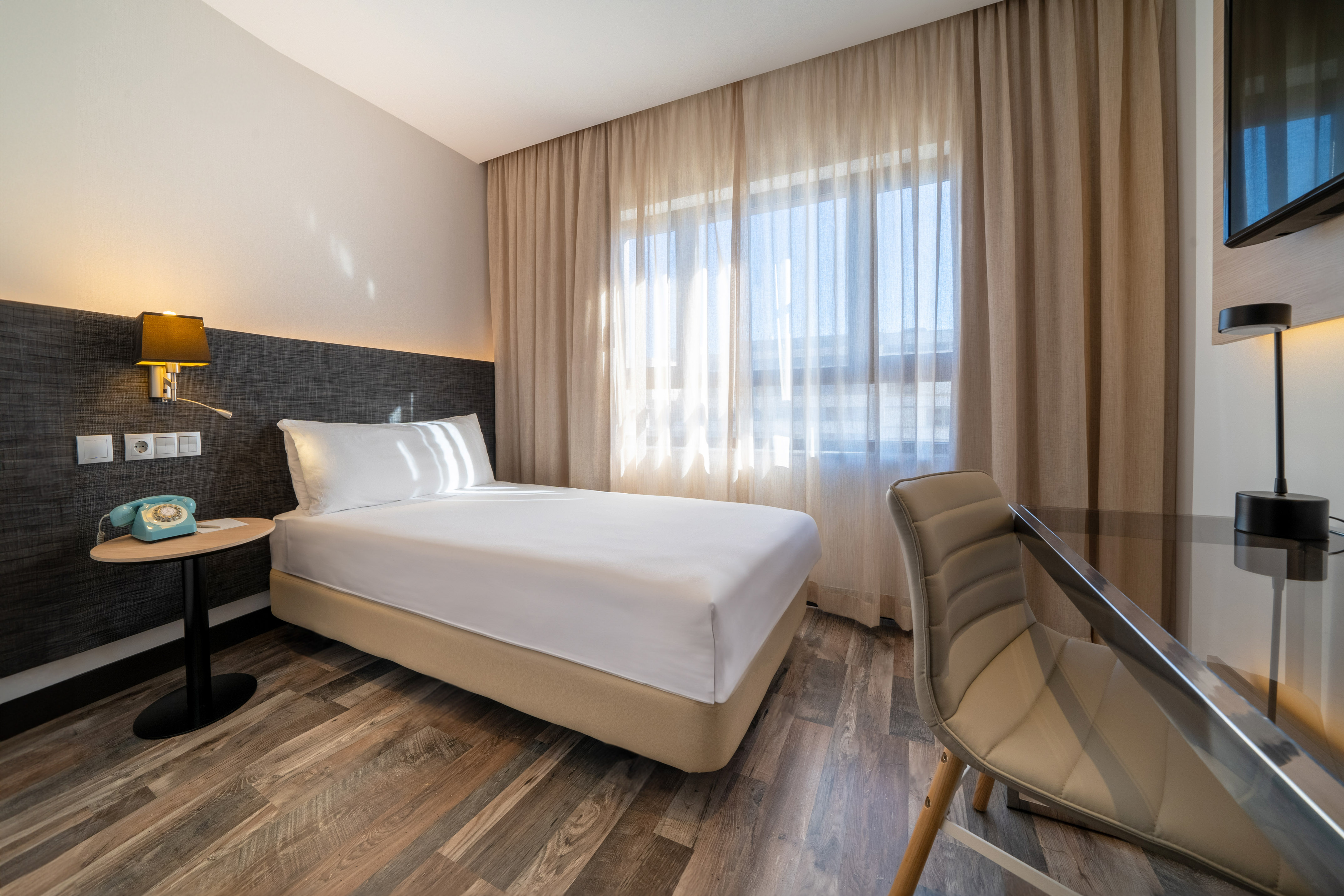 Cozy modern hotel room featuring a single bed, work desk, and sunlit window.
