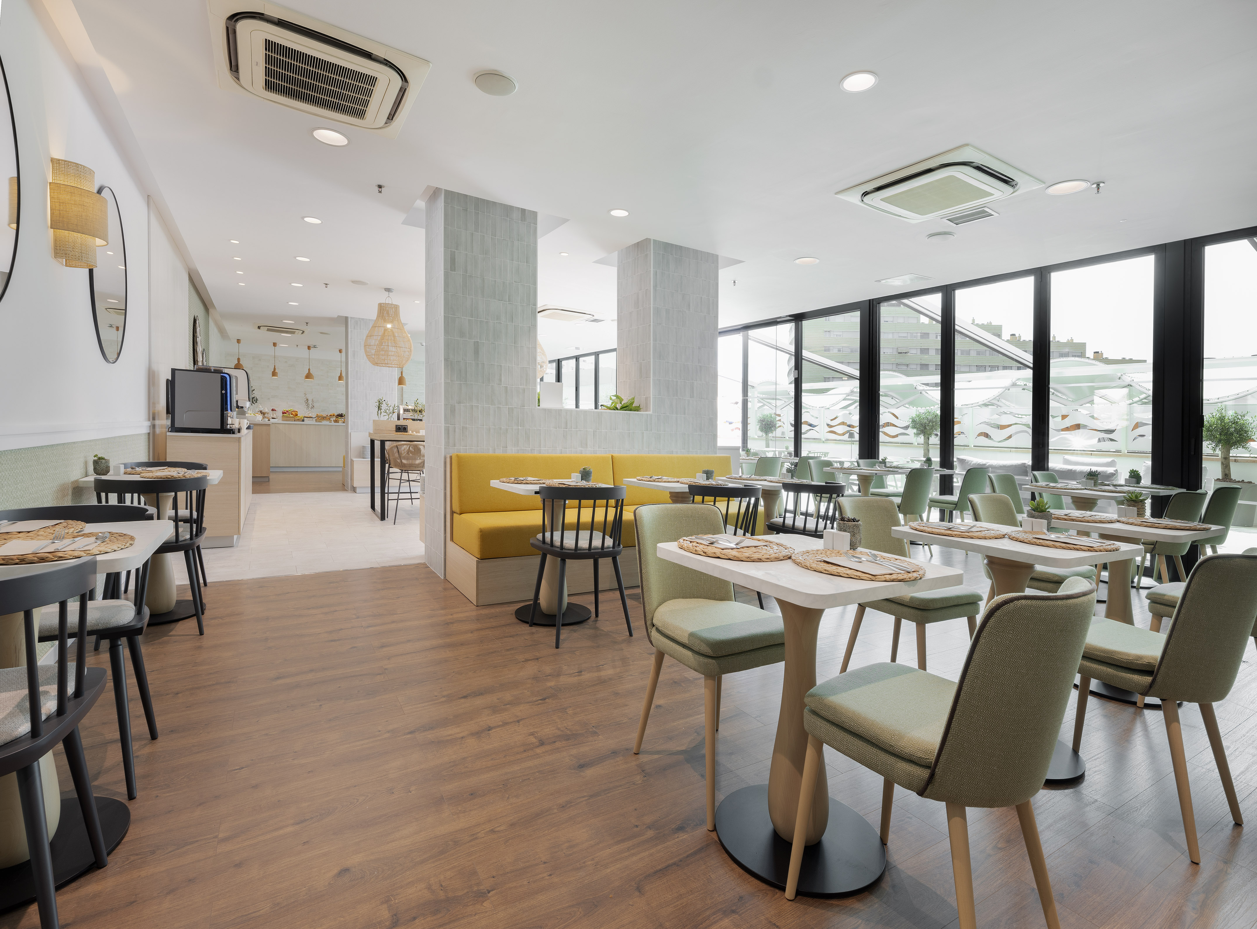 Modern restaurant dining area with yellow booths, green chairs, and large windows.