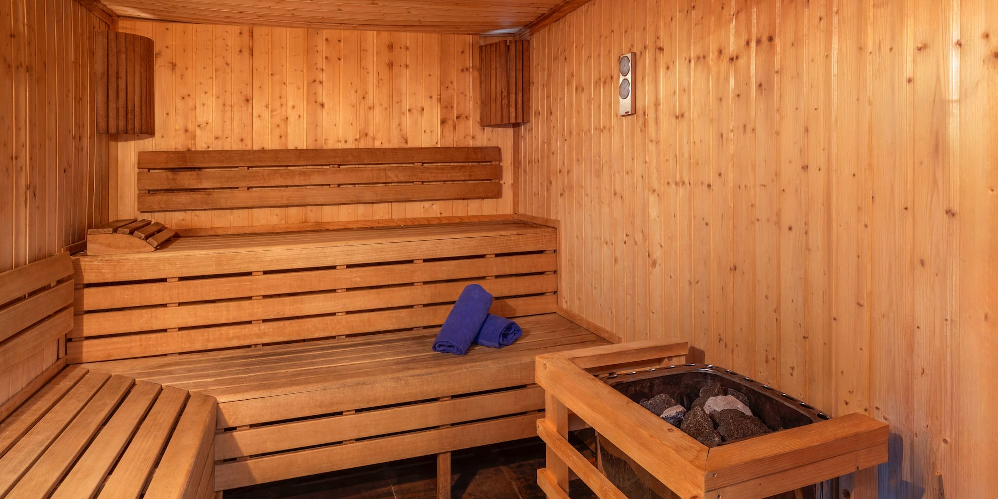 Wooden sauna interior with benches, a stone heater, and blue towels.