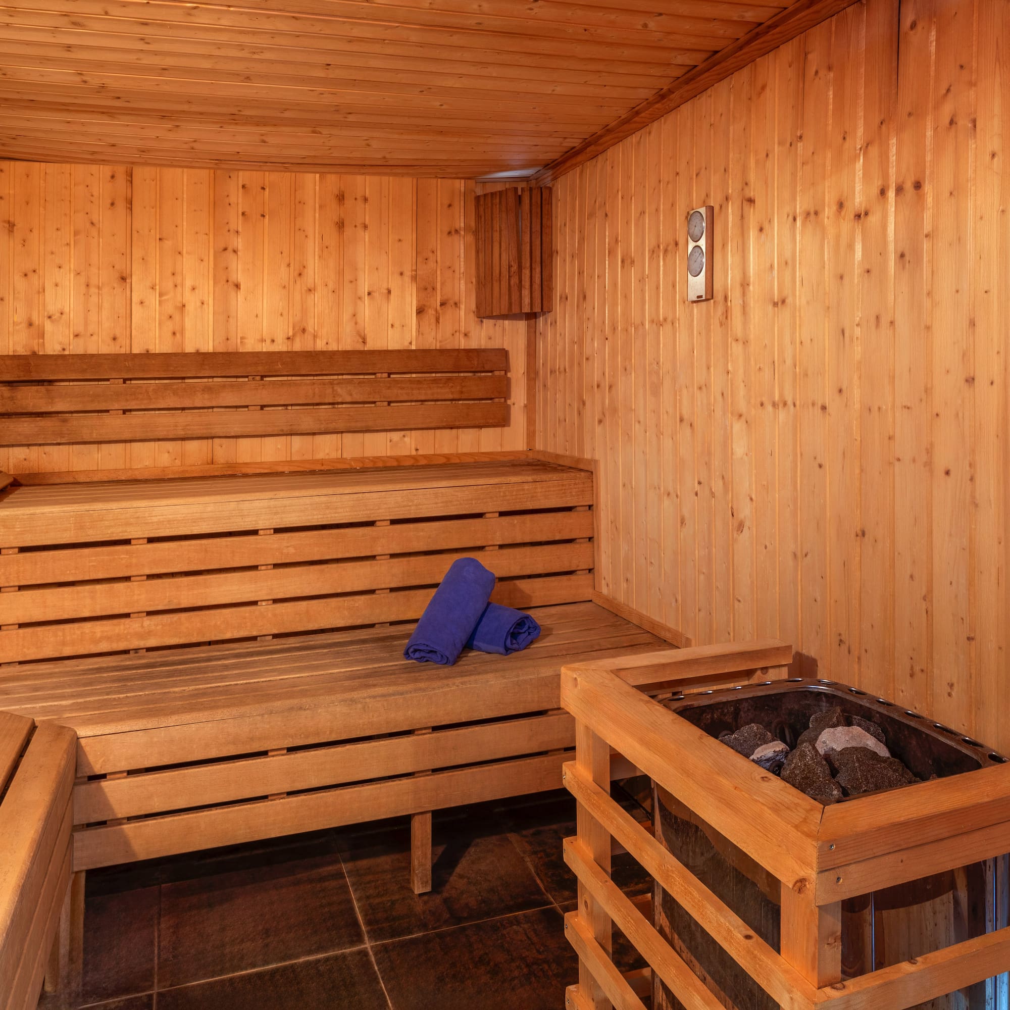 Wooden sauna interior with benches, a stone heater, and blue towels.