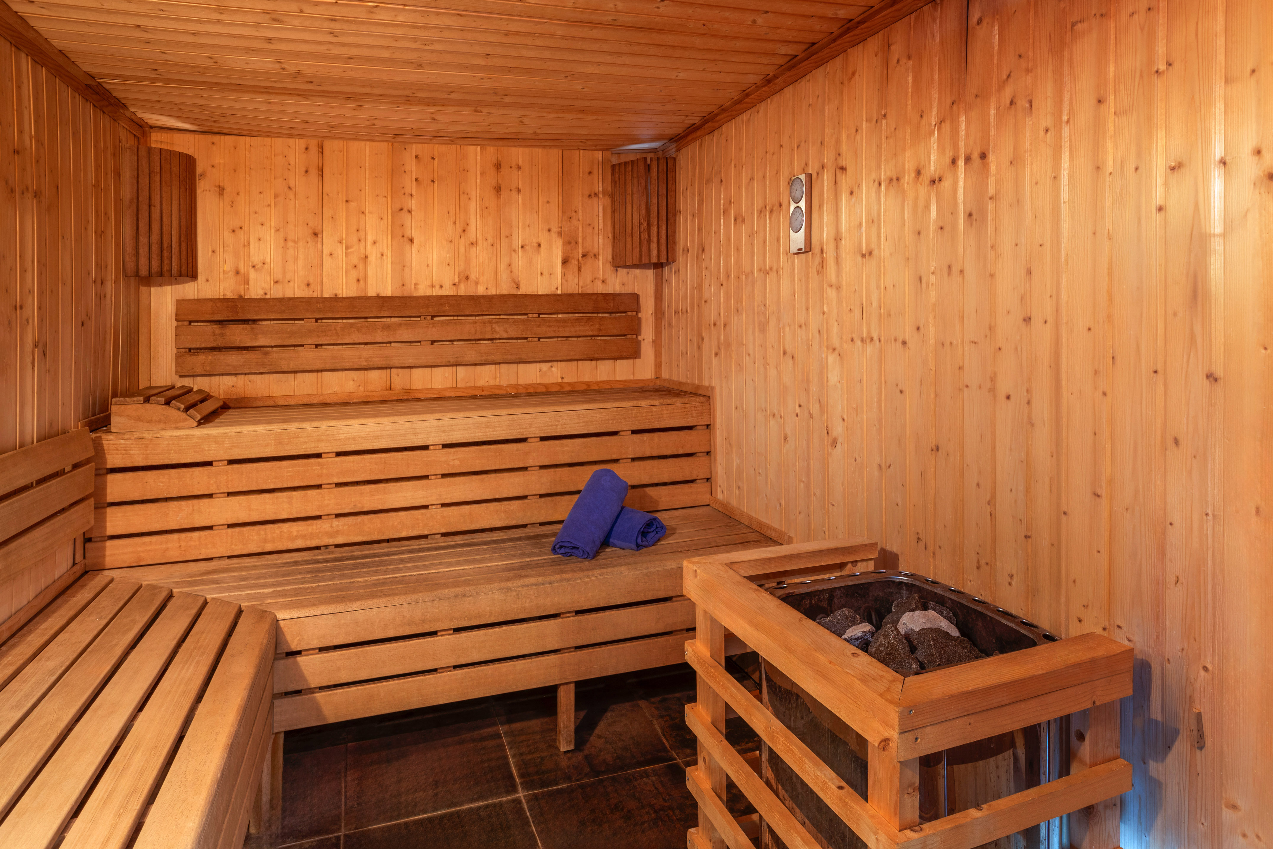Wooden sauna interior with benches, a stone heater, and blue towels.