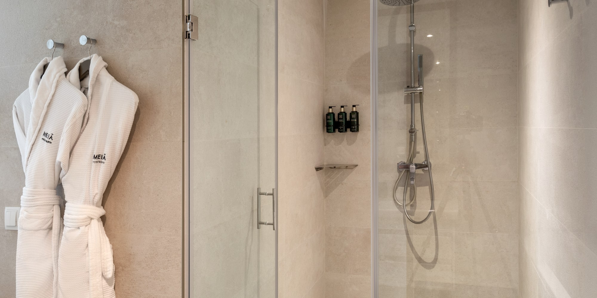 Modern hotel bathroom shower with Meliá bathrobes and amenities.