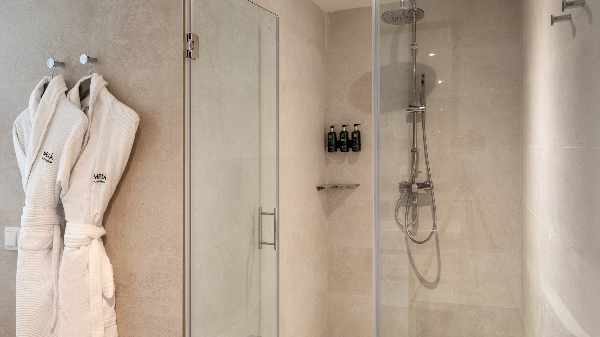 Modern hotel bathroom shower with Meliá bathrobes and amenities.