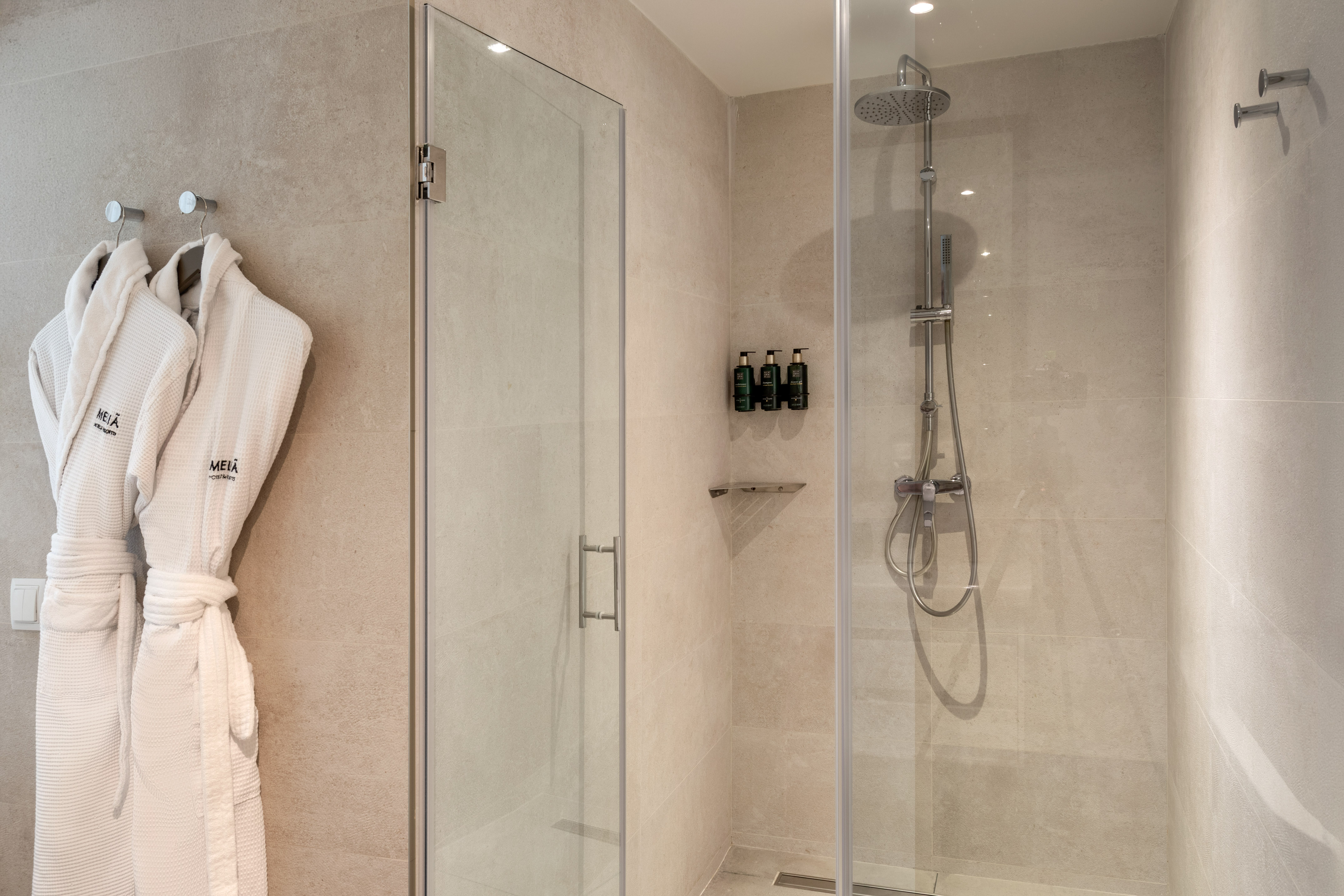 Modern hotel bathroom shower with Meliá bathrobes and amenities.