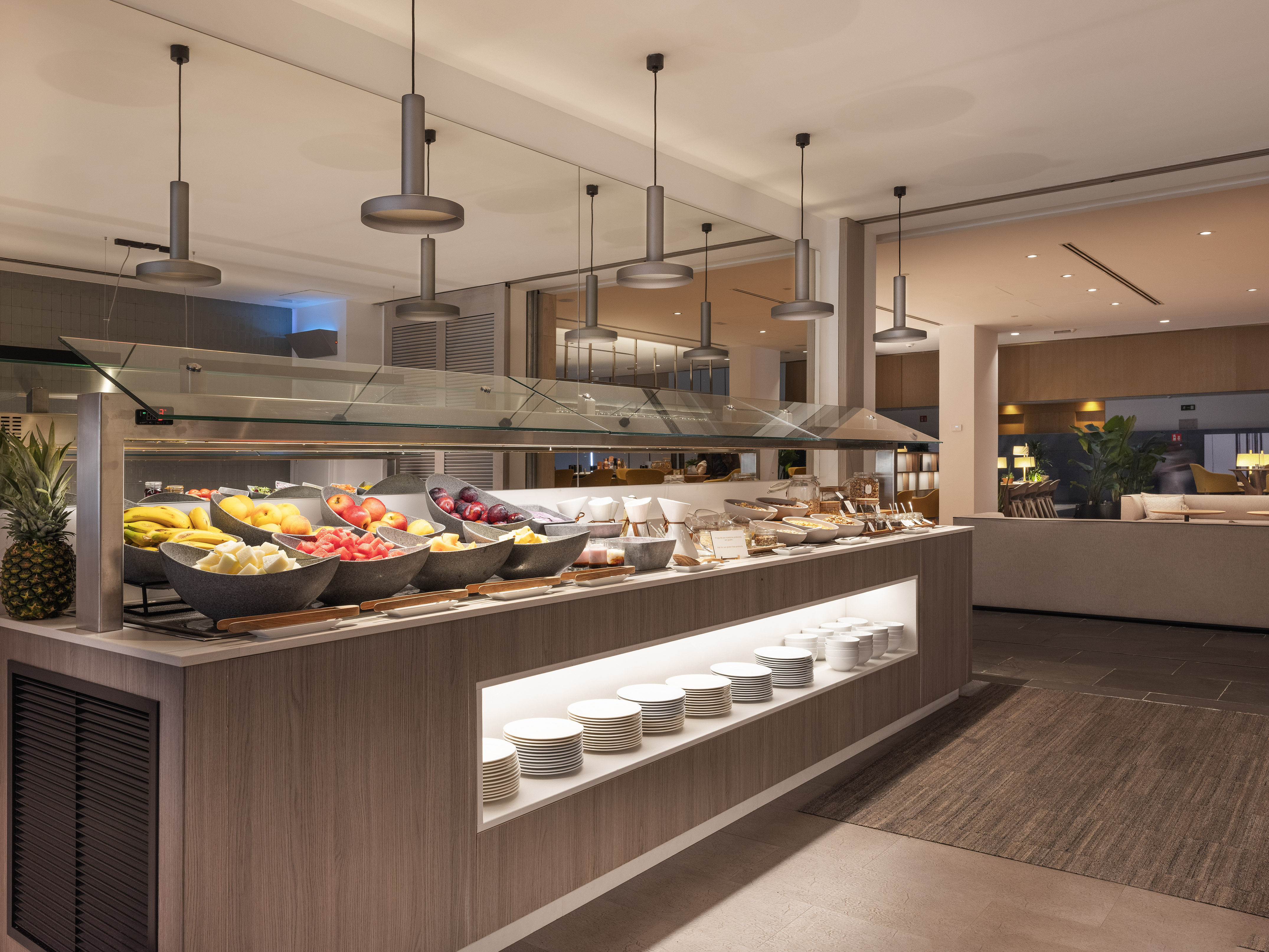 Modern hotel breakfast buffet featuring fresh fruit and stacked plates.
