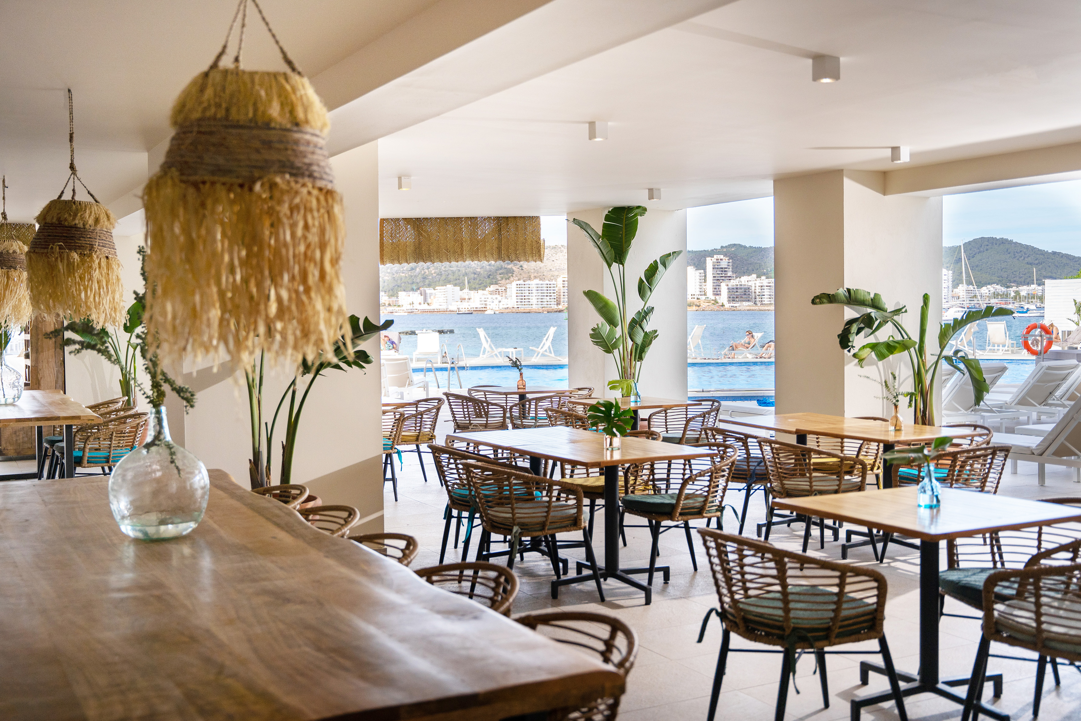 Tropical restaurant with rattan chairs, wooden tables, sea and pool view.