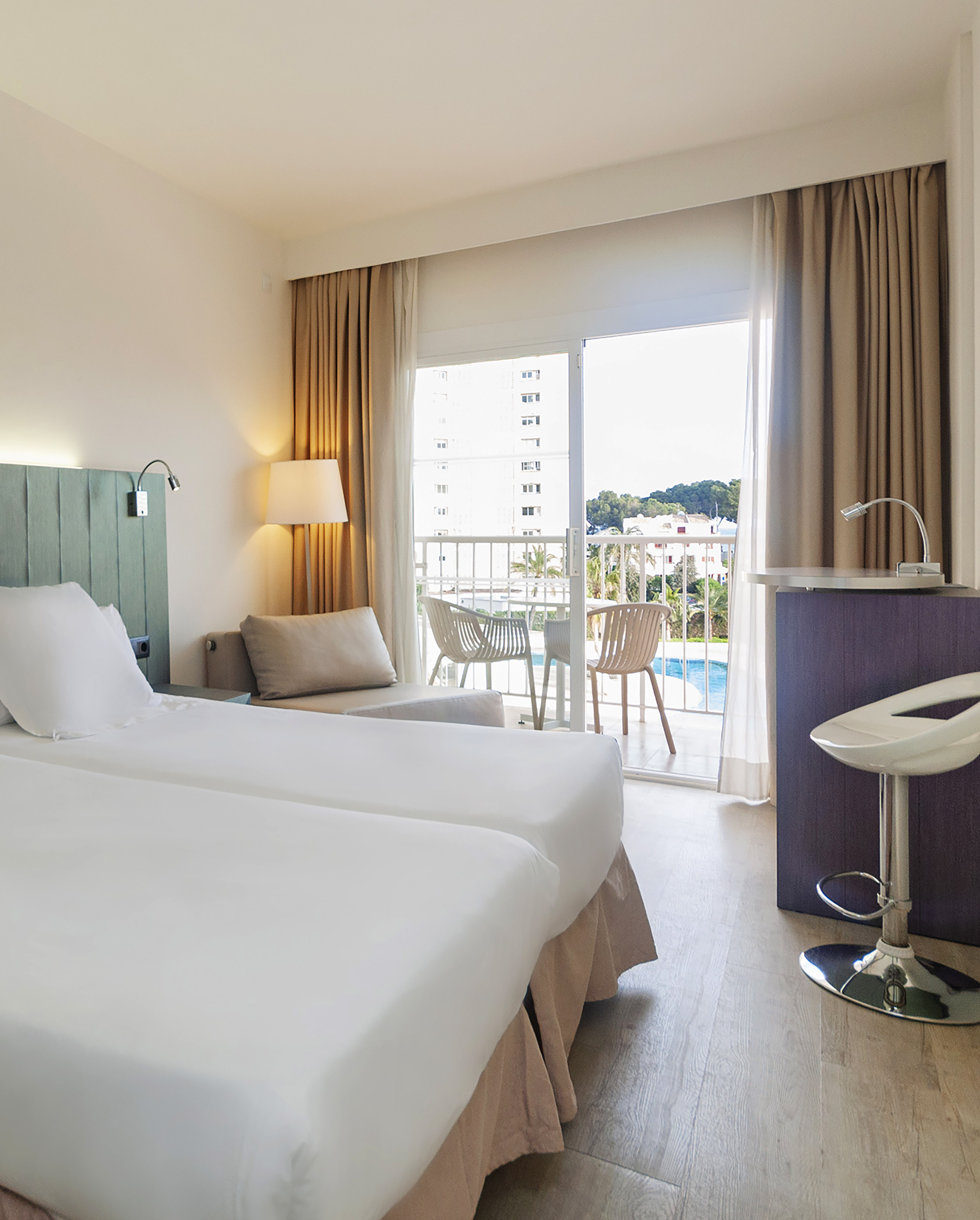 Modern hotel room with twin beds, balcony, pool view, and sofa.