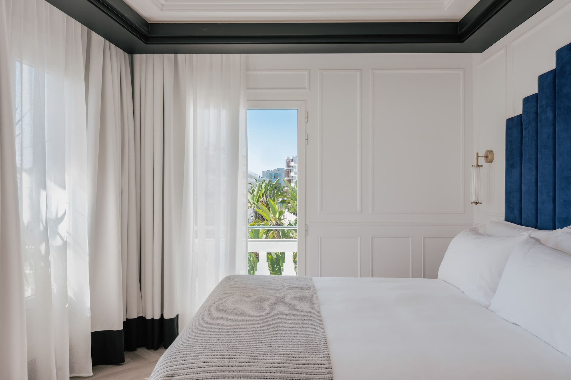 Luxury white hotel bedroom with blue headboard and balcony view.