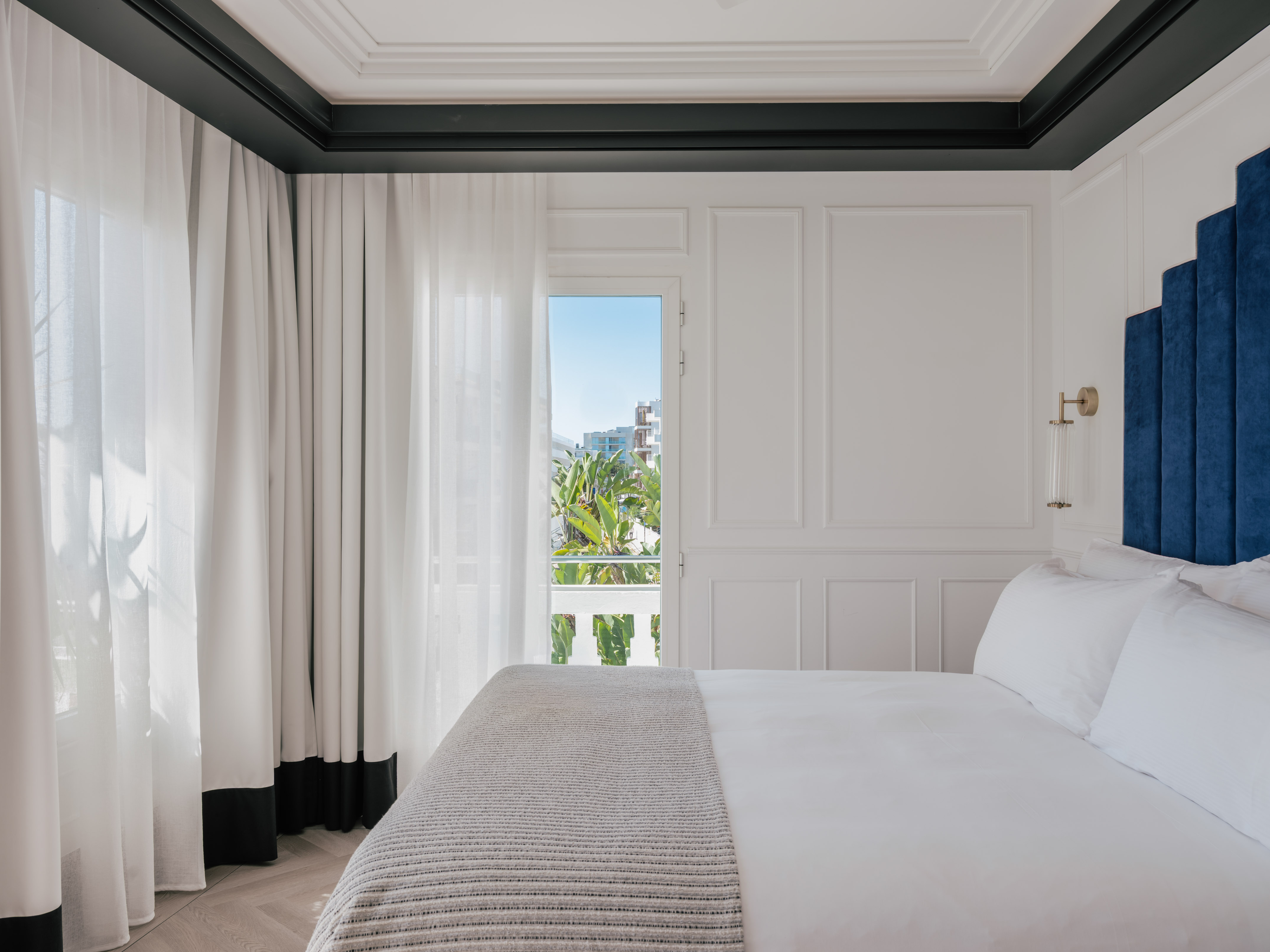 Luxury white hotel bedroom with blue headboard and balcony view.