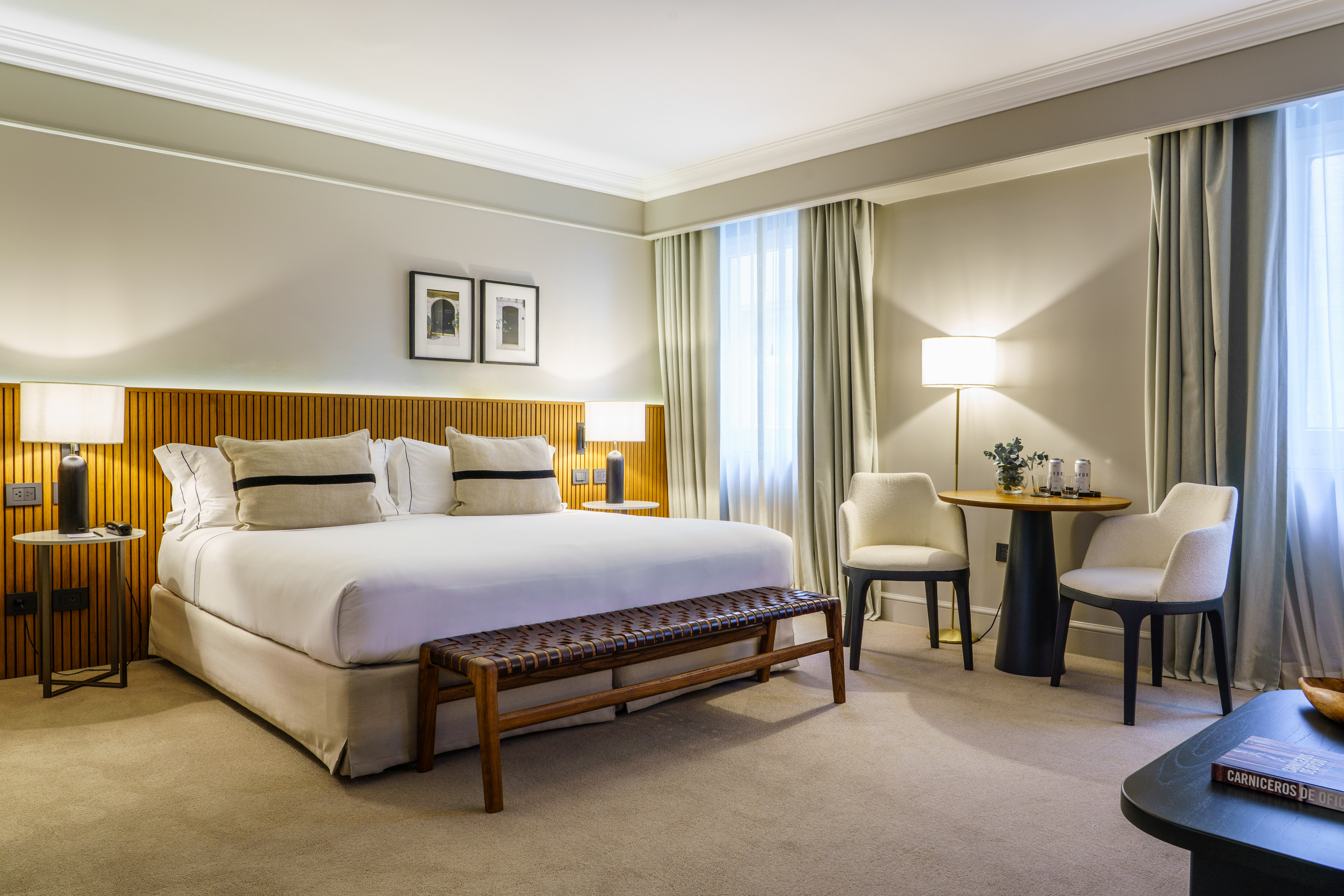 Elegant hotel bedroom with king bed, wooden headboard, and cozy seating.