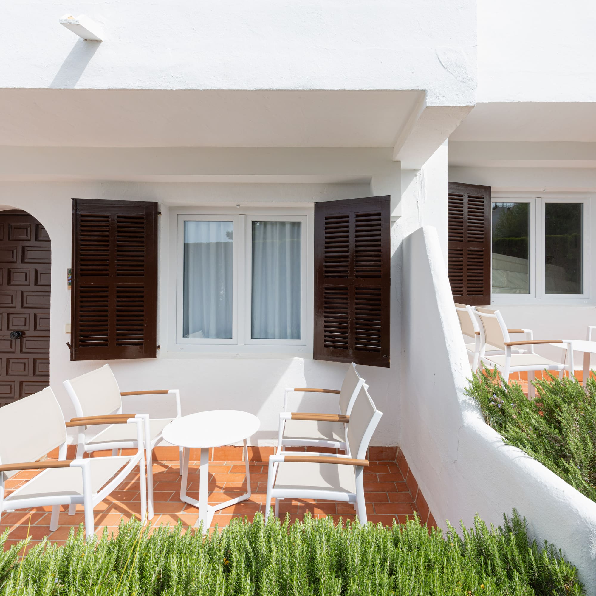 White Mediterranean patio with brown shutters, arched doors, and outdoor seating.