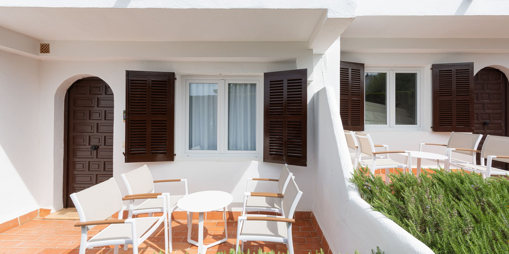 White Mediterranean patio with brown shutters, arched doors, and outdoor seating.