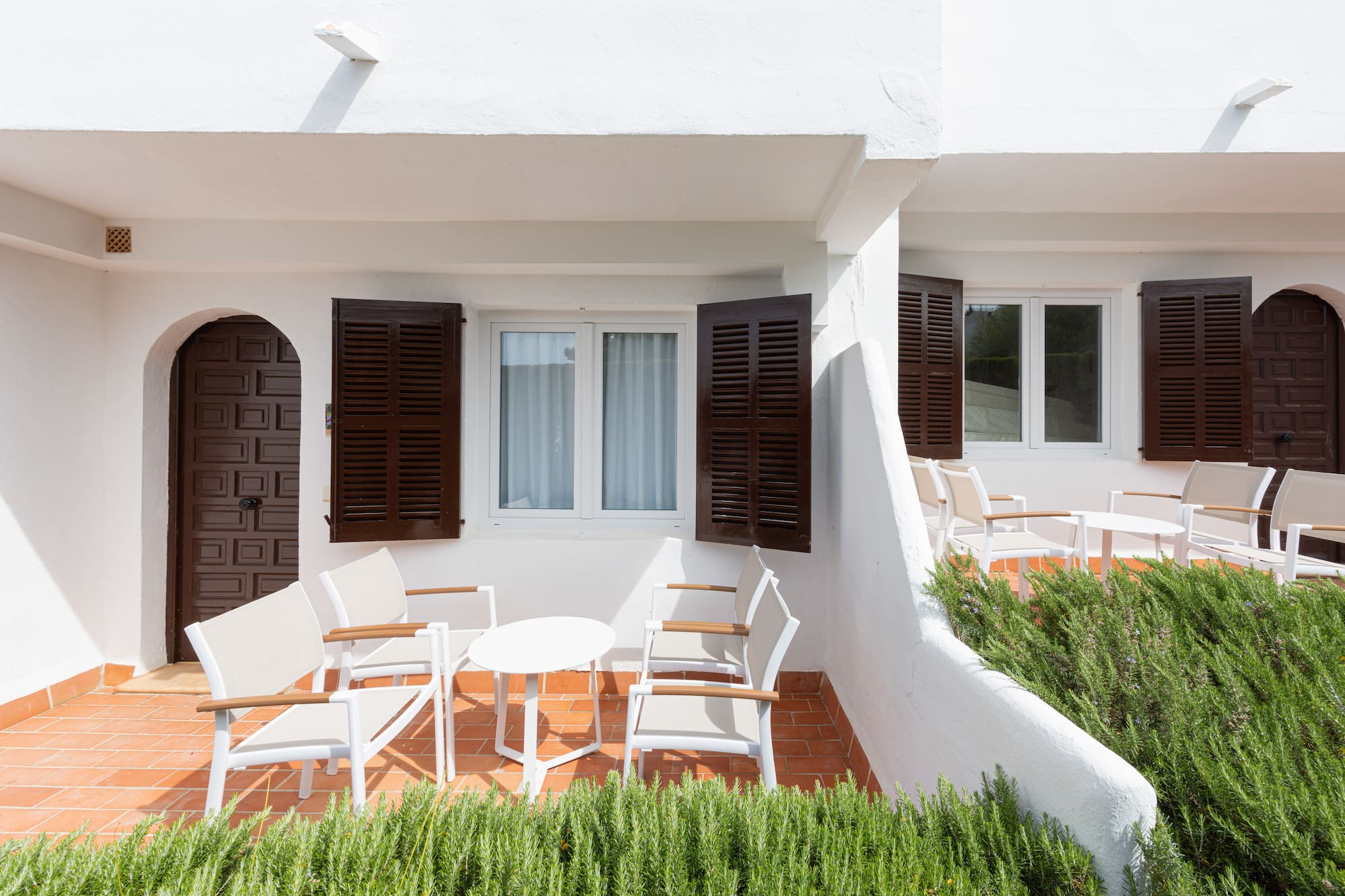 White Mediterranean patio with brown shutters, arched doors, and outdoor seating.