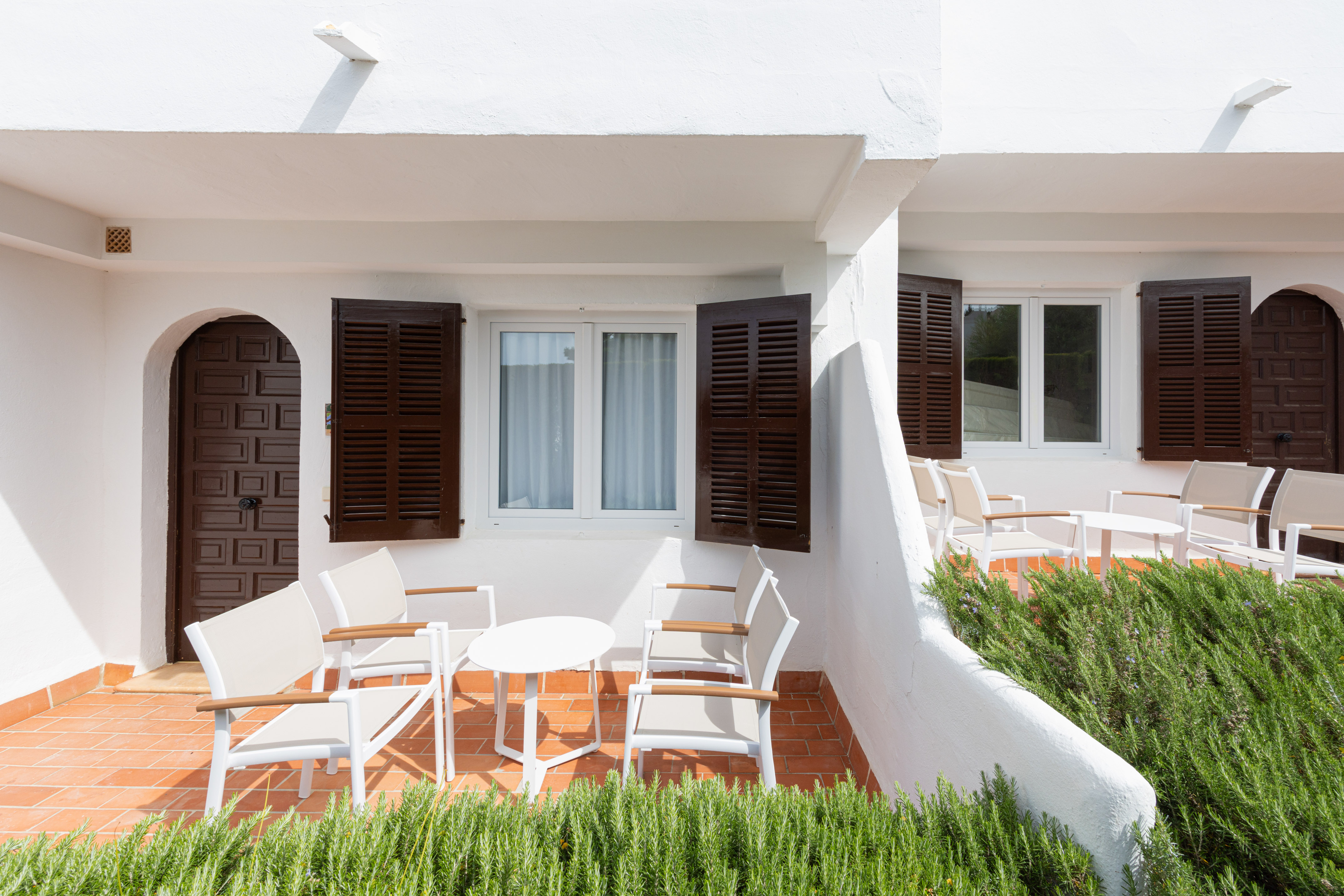 White Mediterranean patio with brown shutters, arched doors, and outdoor seating.