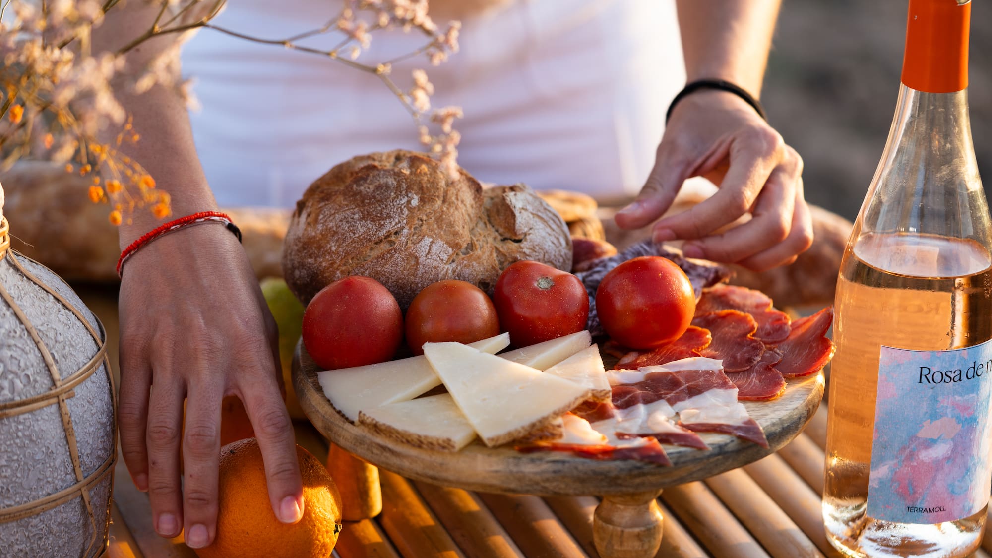 Picnic español con embutidos, queso, pan, tomates y vino rosado al atardecer.