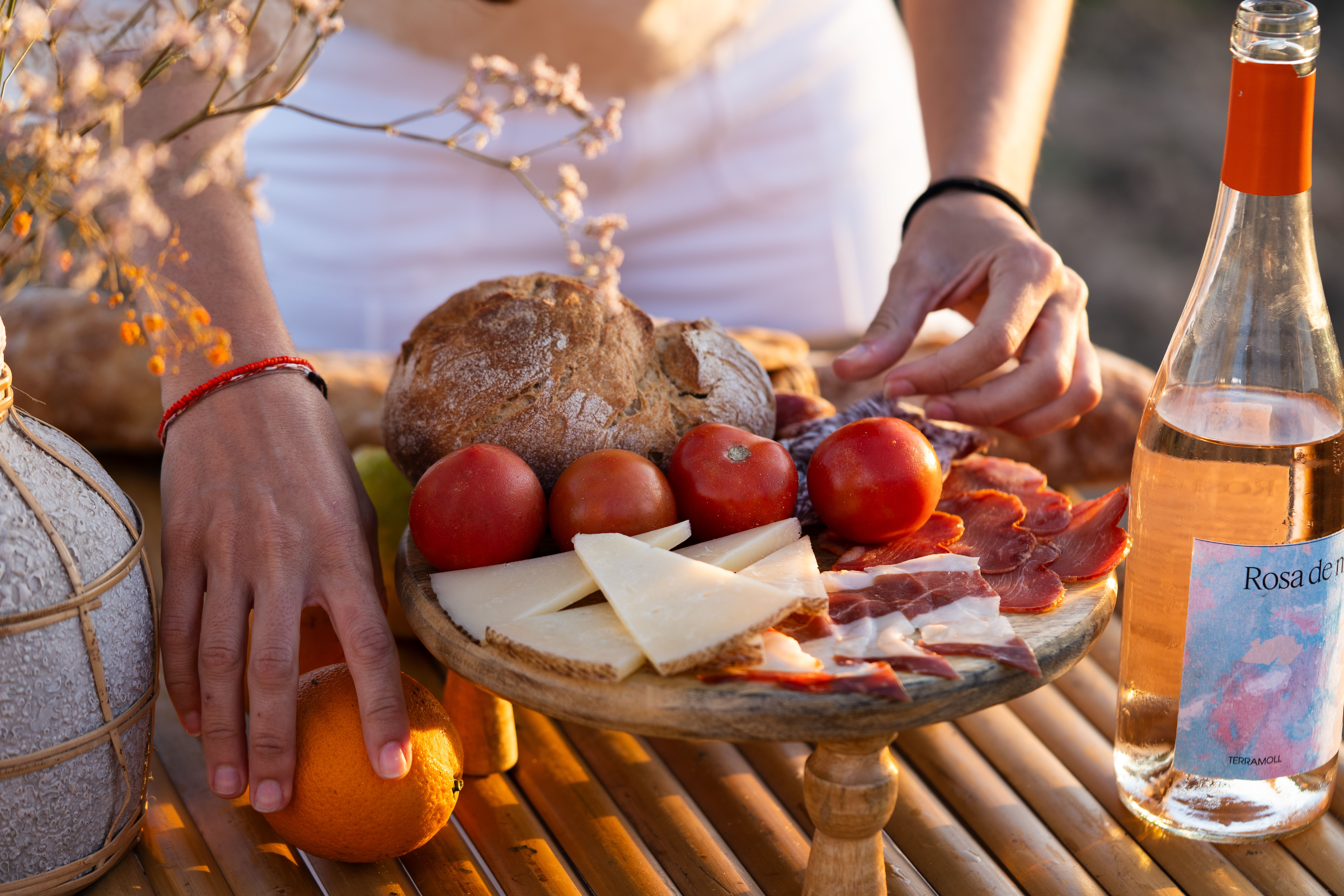Picnic español con embutidos, queso, pan, tomates y vino rosado al atardecer.