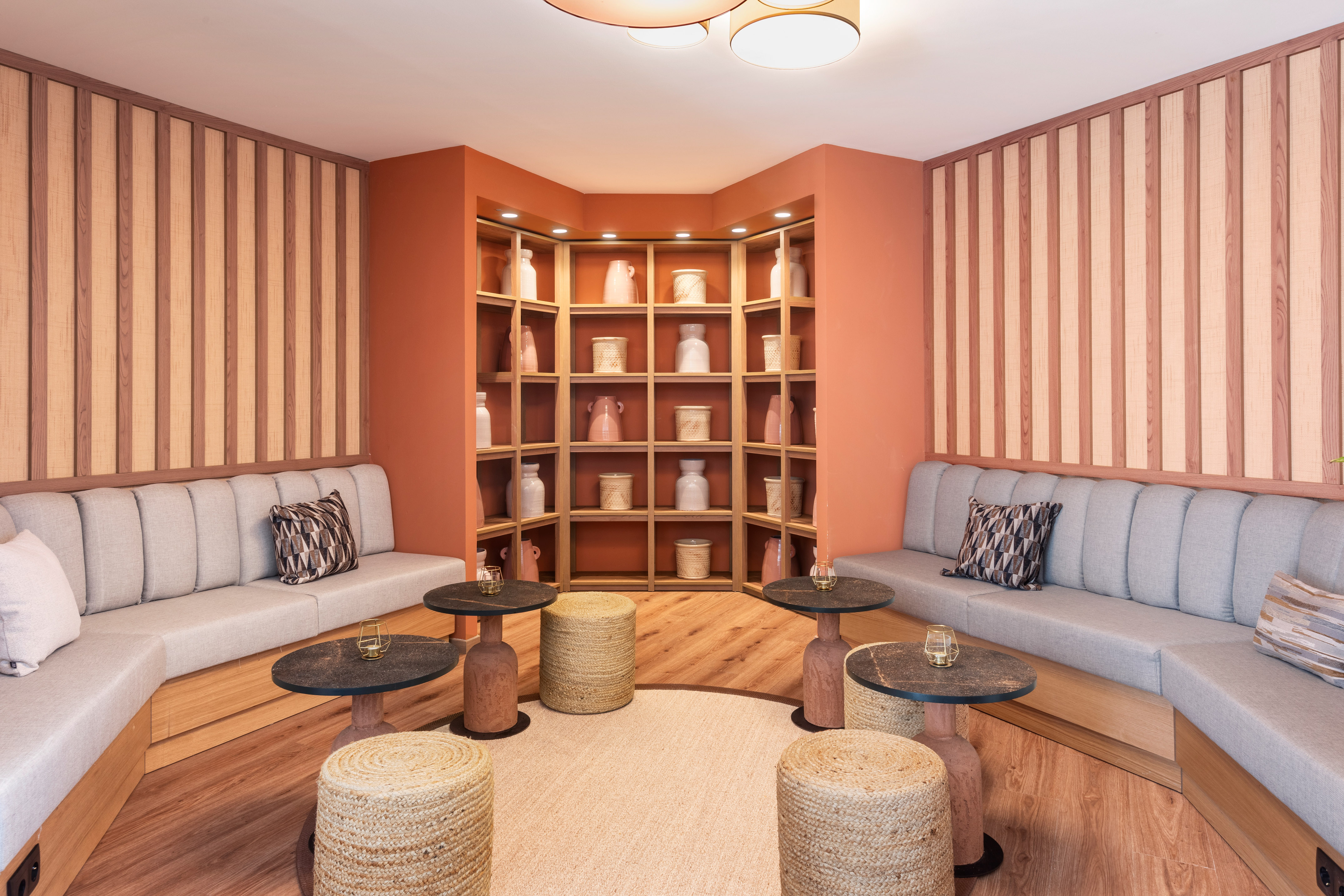 Modern lounge with terracotta wall shelves, wood panels, gray booth seating.