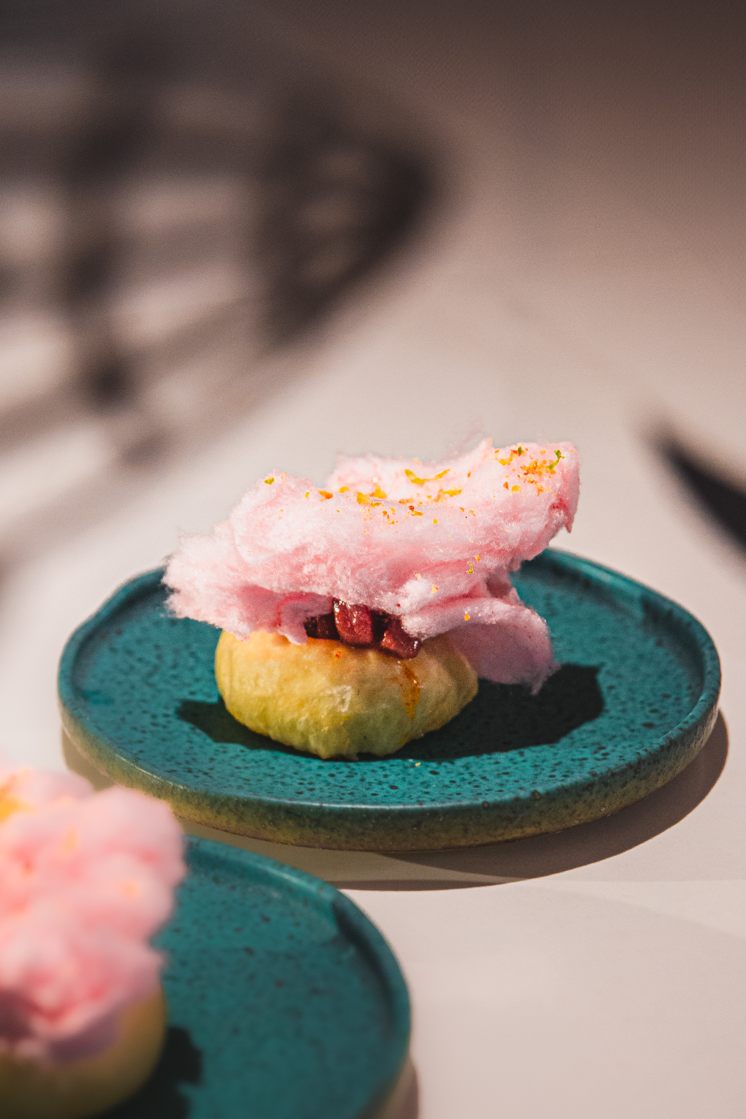 Pink cotton candy dessert with pastry, fruit, and zest on a teal plate.