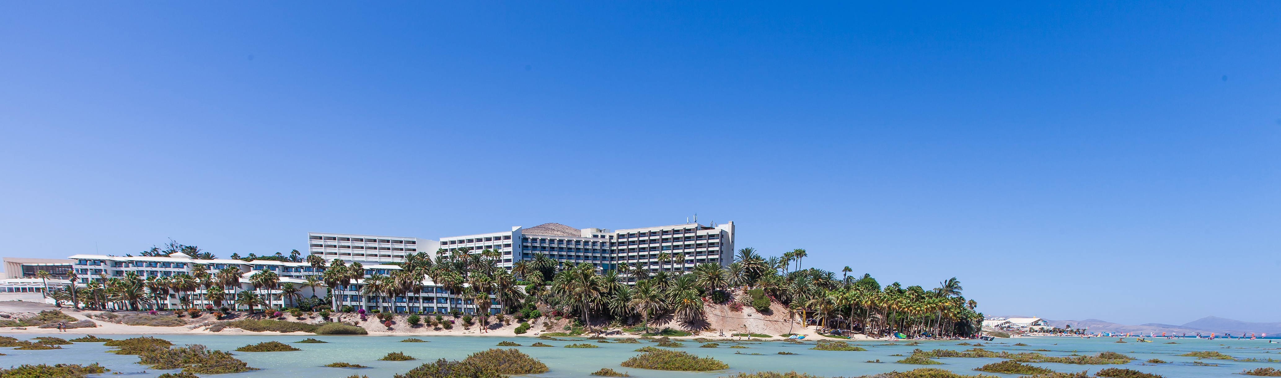 Coastal hotel resort with palm trees overlooking a turquoise lagoon.