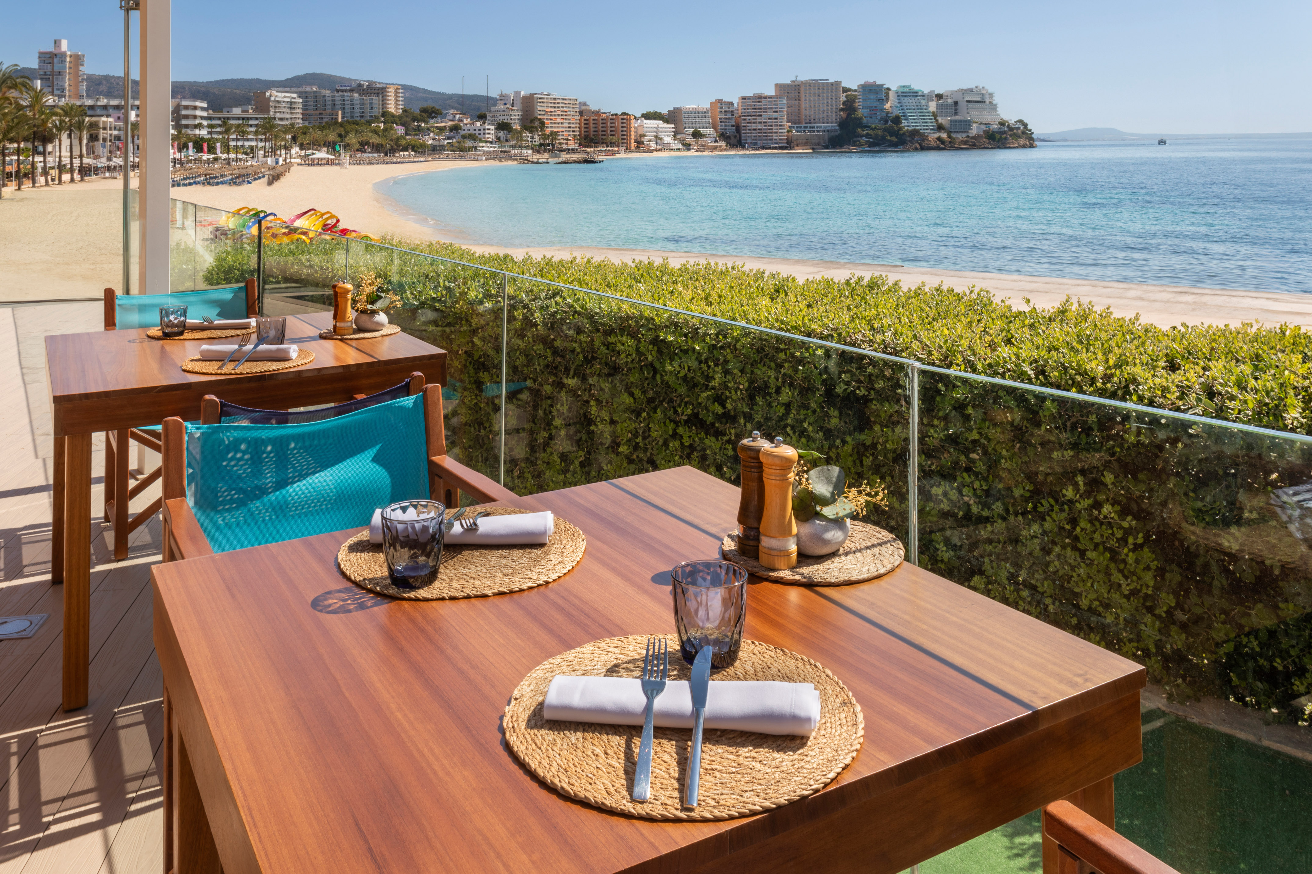 Restaurant terrace overlooking sandy beach, turquoise sea, and coastal city.