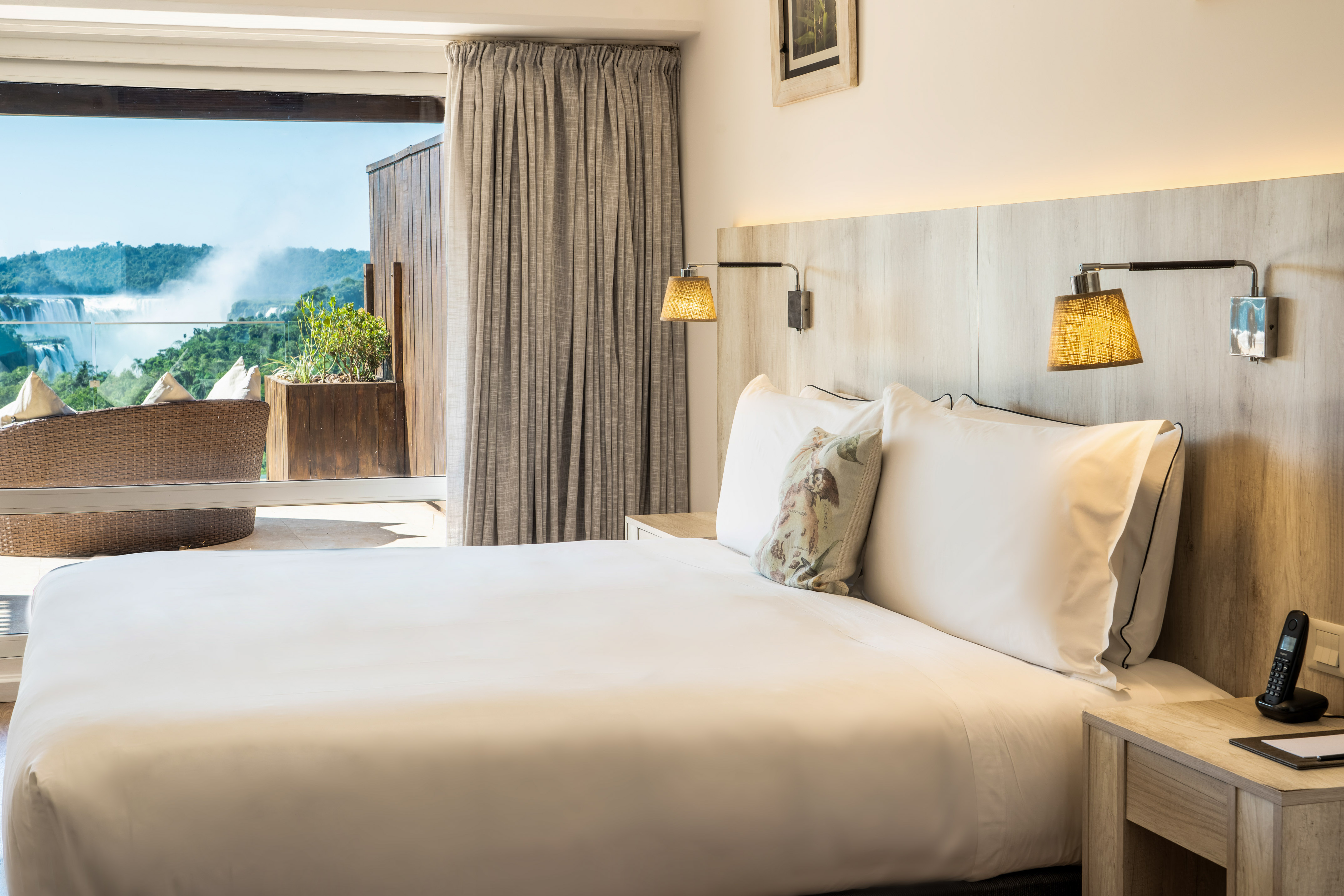 Luxury hotel bedroom with balcony overlooking Iguazu Falls and lush nature.