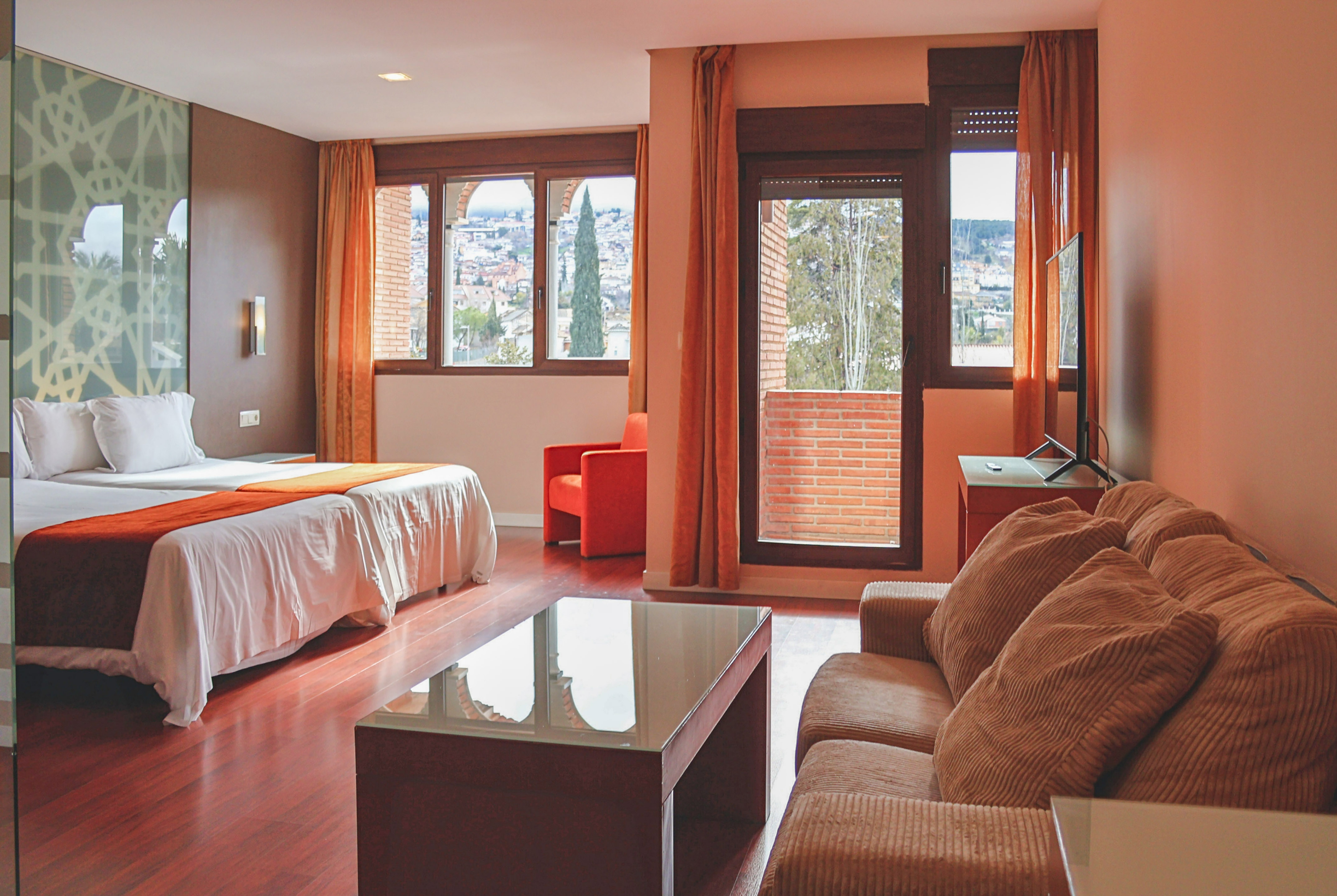 Modern hotel suite with twin beds, sofa, and a scenic city view.
