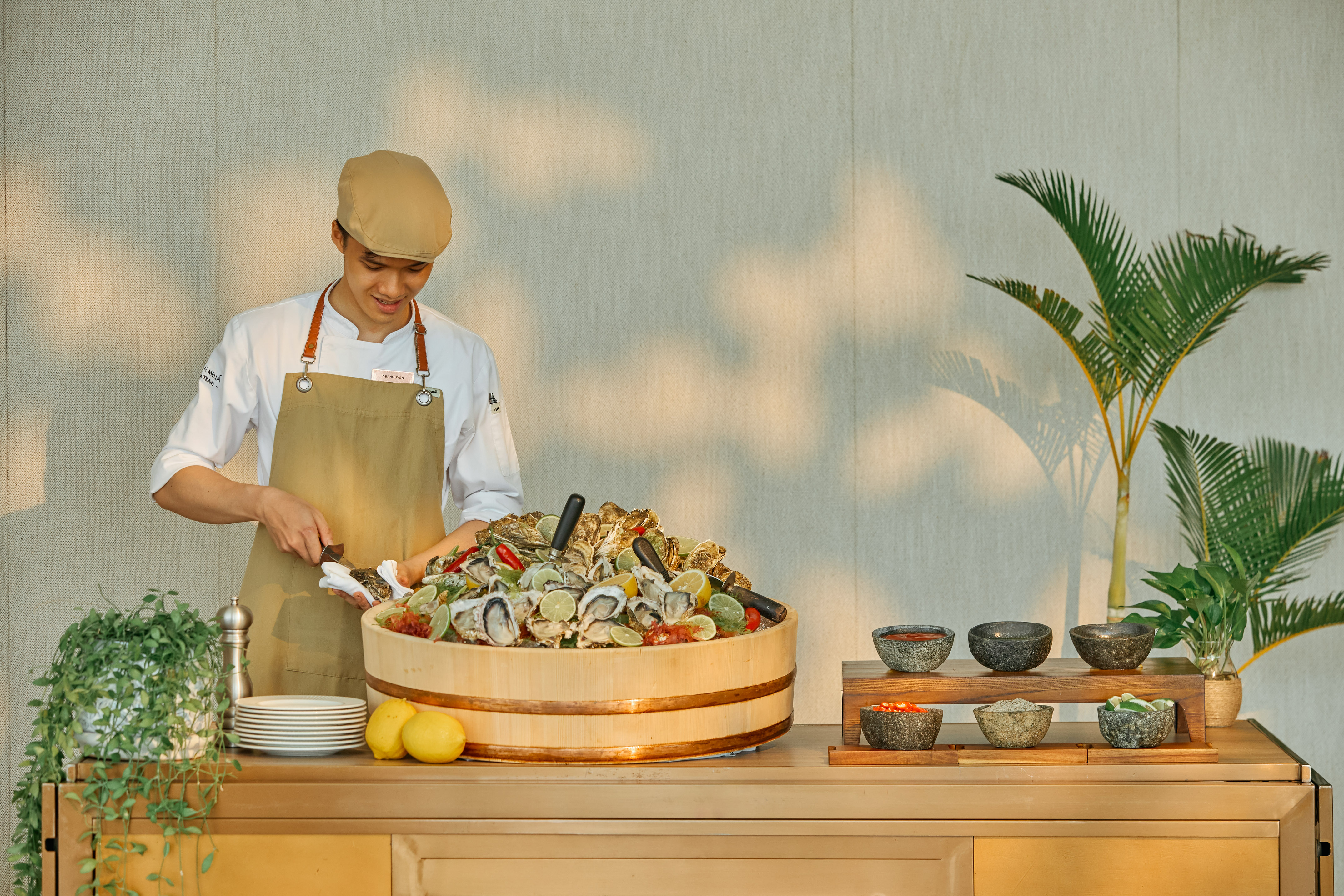 Chef shucking fresh oysters at a seafood buffet with limes and condiments.