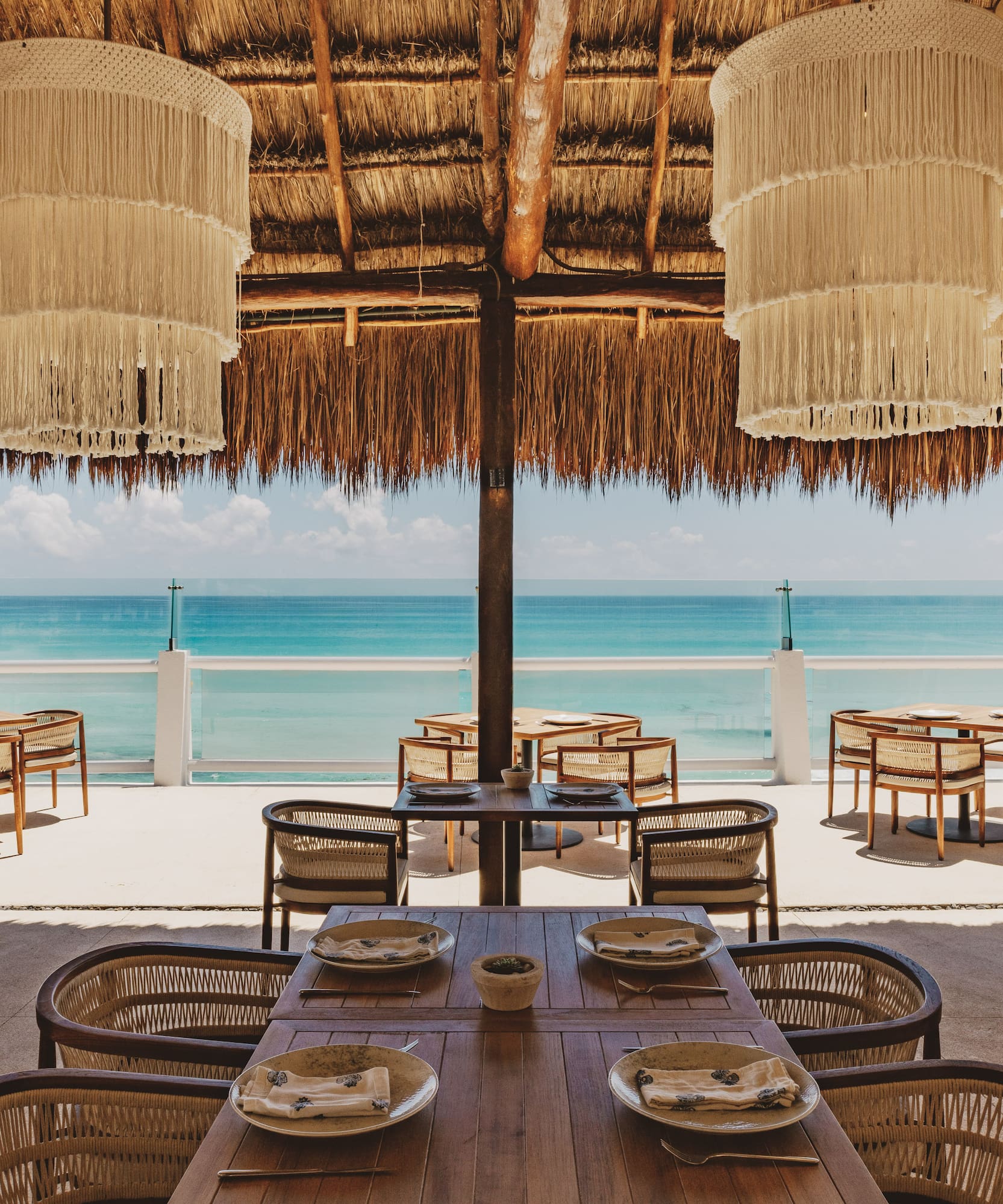 Oceanfront restaurant with thatch roof, macrame chandeliers, and sea view.