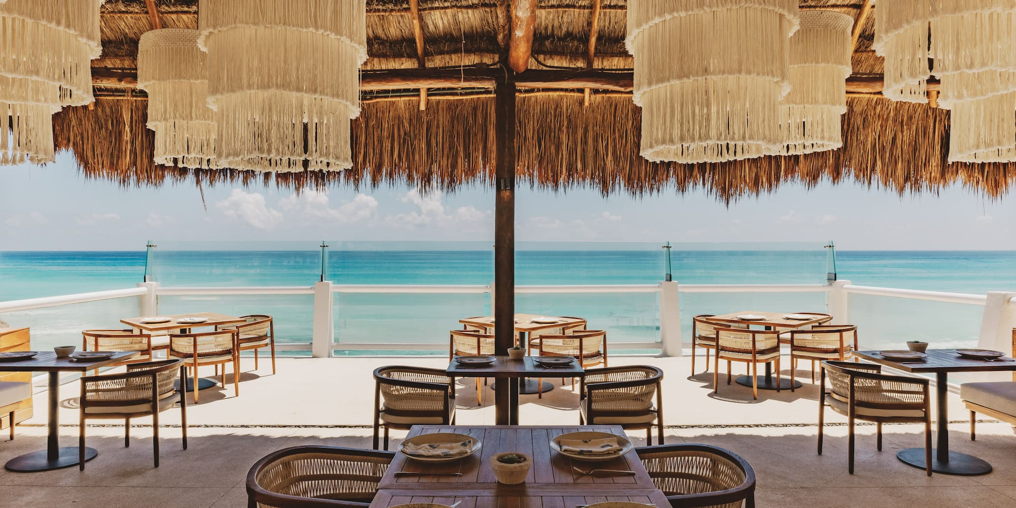 Beachfront restaurant with macrame lights, palapa roof, and turquoise sea.