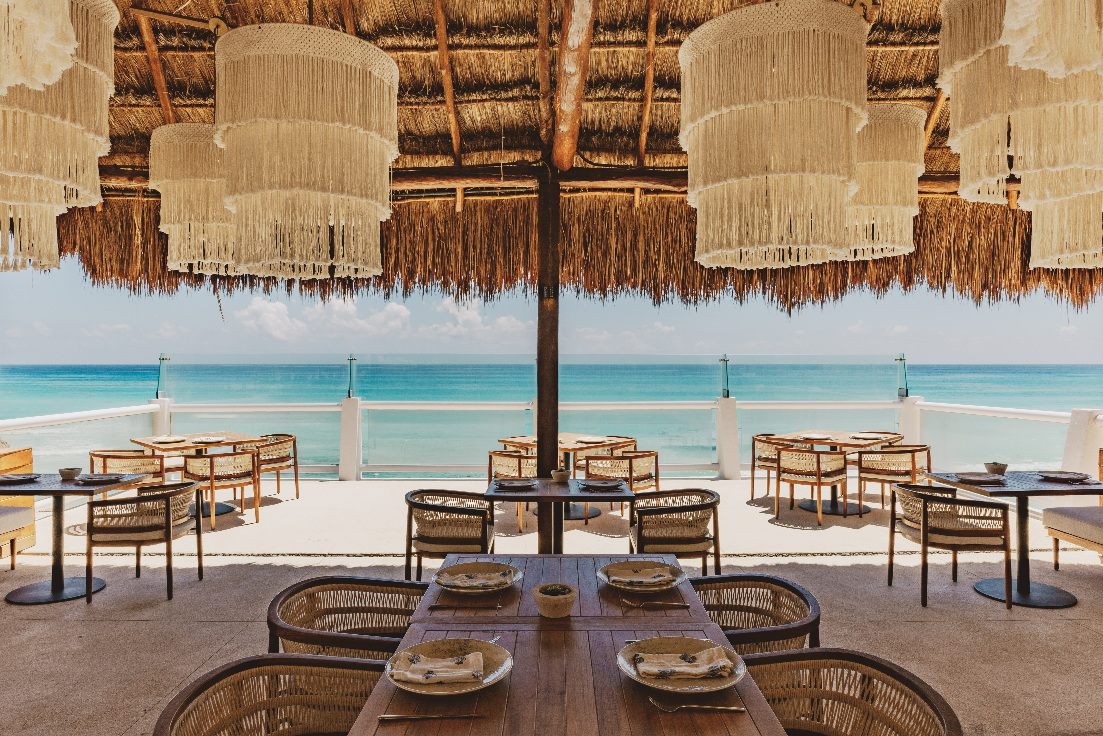 Oceanfront restaurant with thatch roof, macrame chandeliers, and sea view.