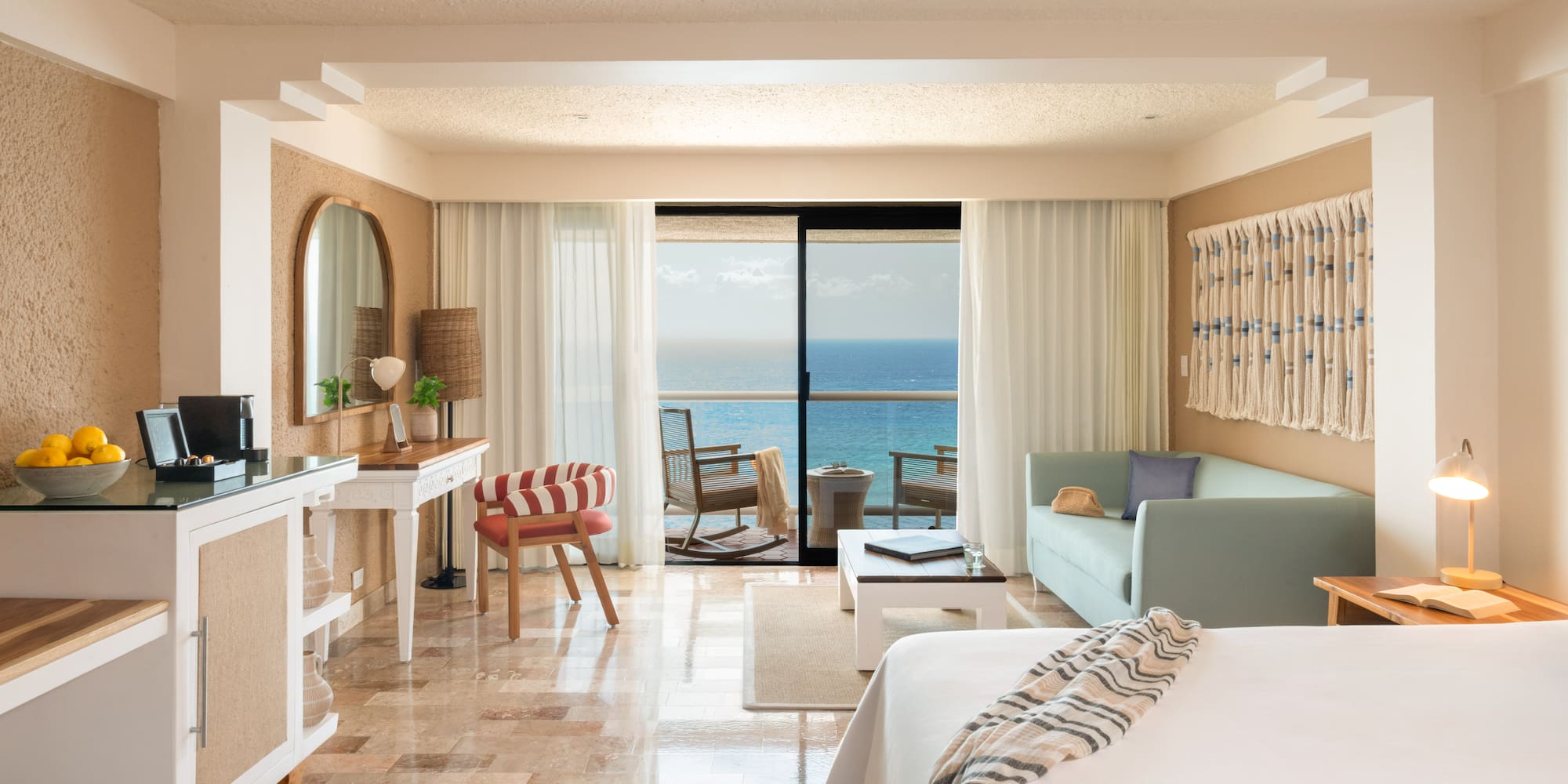 Ocean view resort suite with balcony, bed, sofa, and tropical decor.