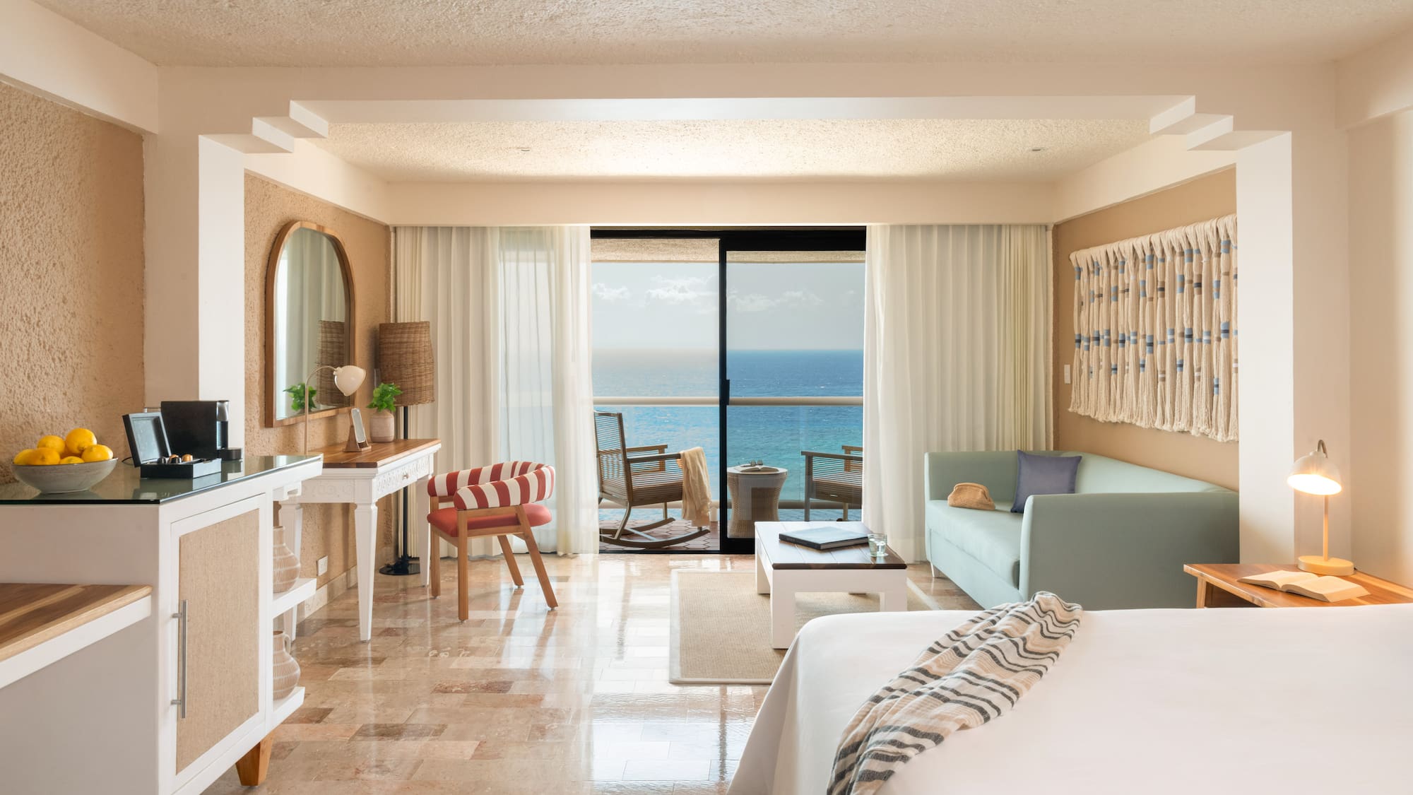 Ocean view resort suite with balcony, bed, sofa, and tropical decor.