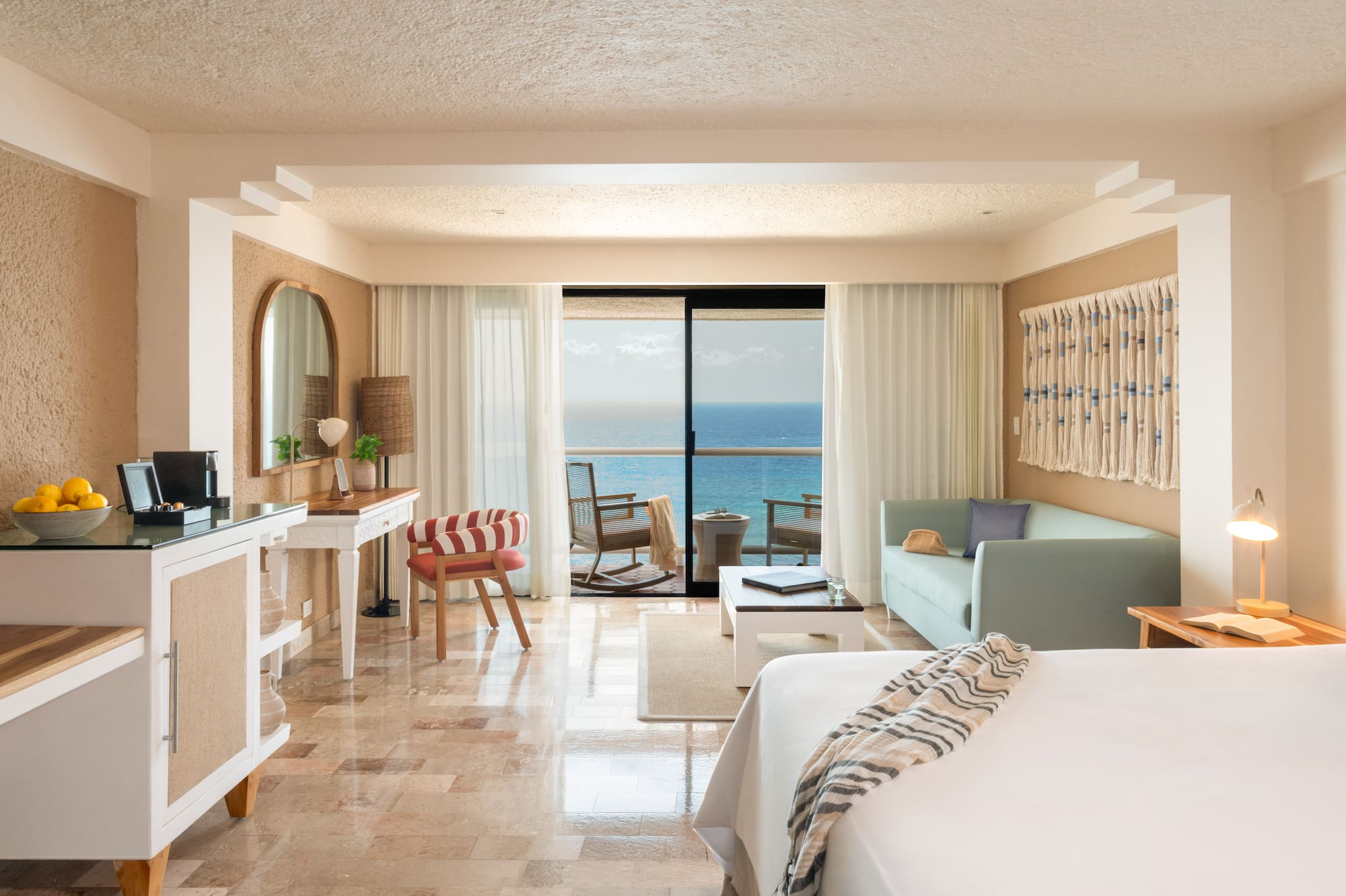 Ocean view resort suite with balcony, bed, sofa, and tropical decor.