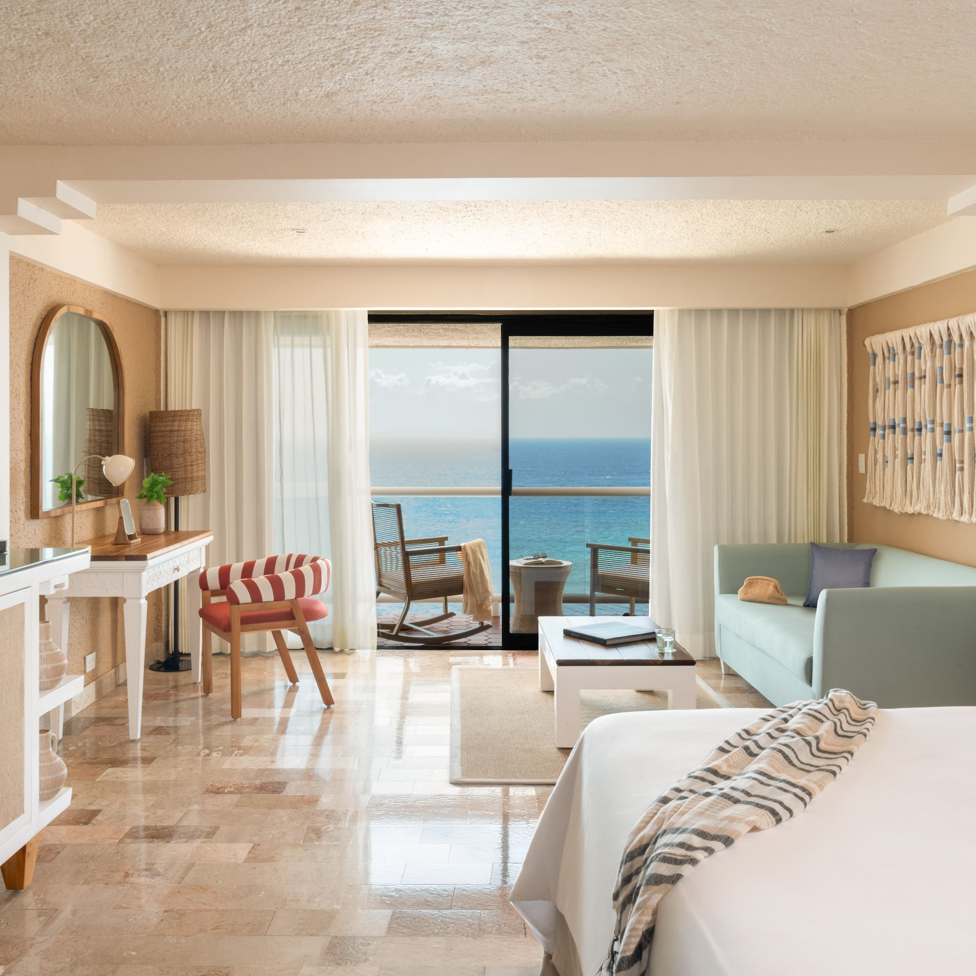 Ocean view resort suite with balcony, bed, sofa, and tropical decor.