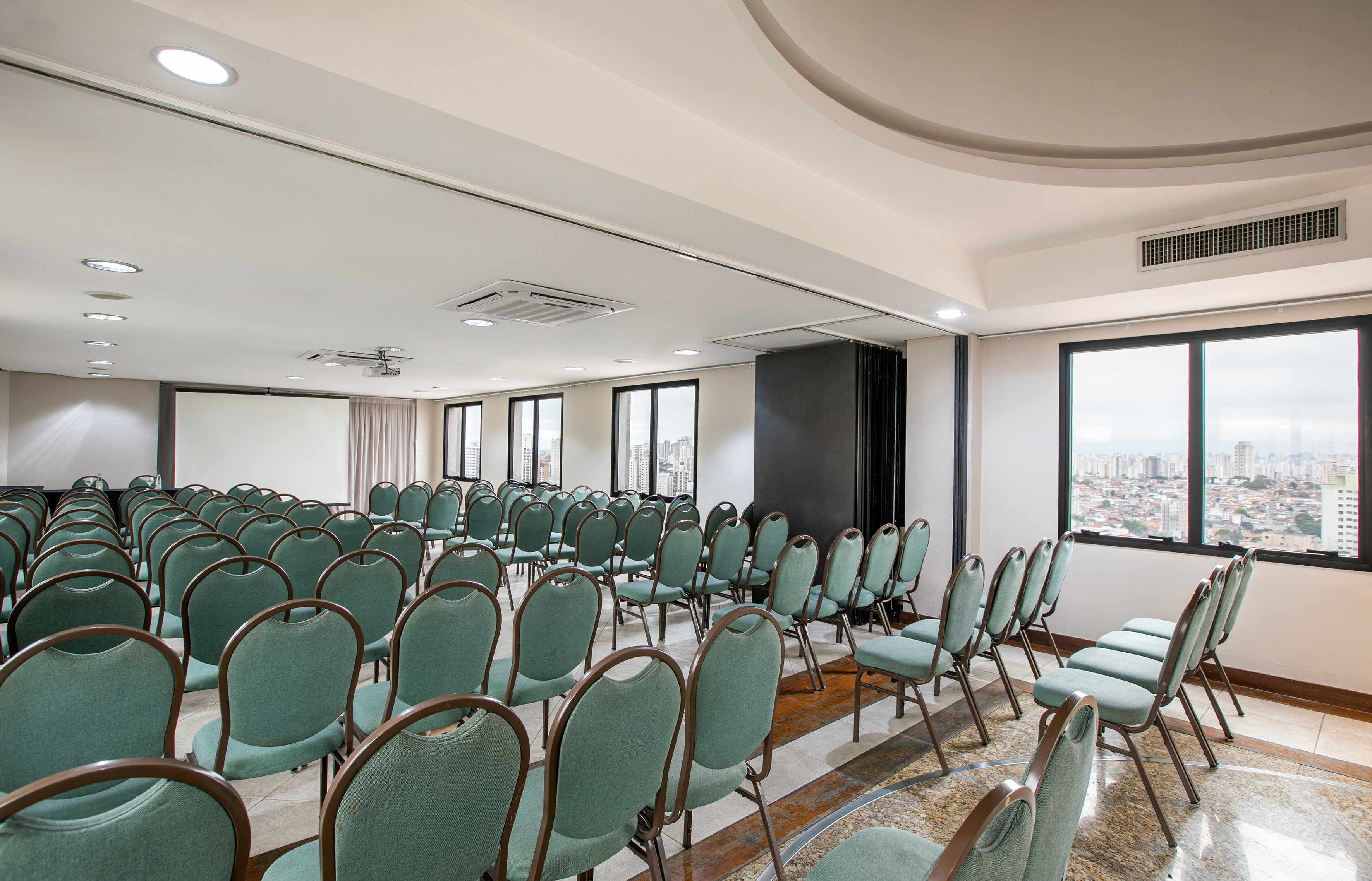 Empty conference room with green chairs, projector screen, and city view.