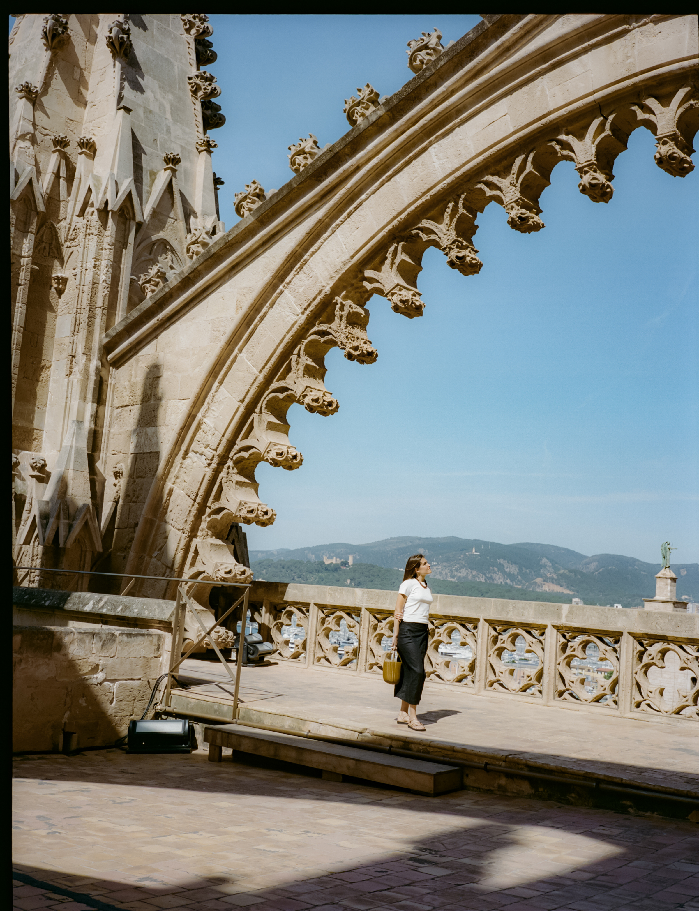 Woman on a gothic cathedral balcony overlooking a city and mountains.