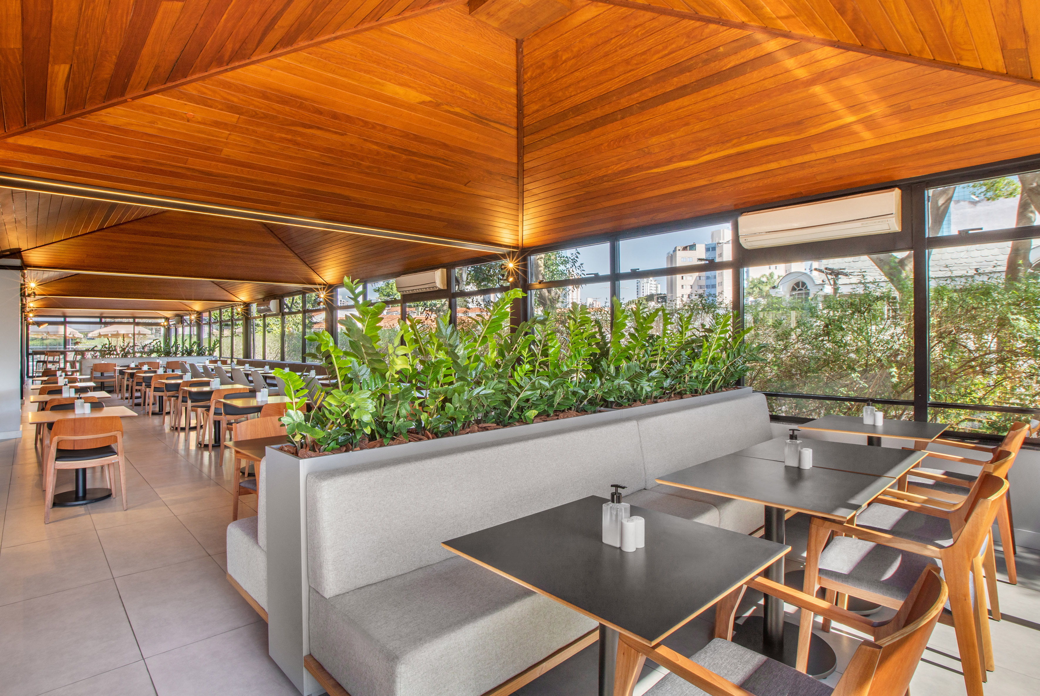 Bright restaurant dining area featuring wooden ceiling and lush indoor plants.